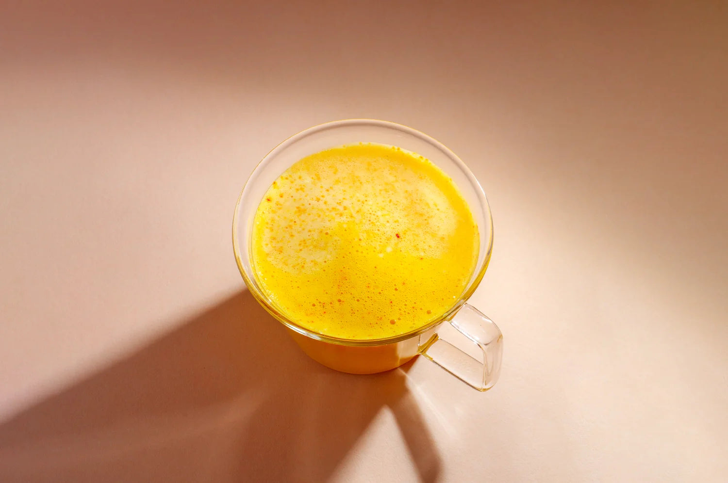 A captivating shot of THE FULLEST’s Warm Feelings saffron latte, set against a soft tan backdrop with warm, moody lighting, highlighting its rich and soothing yellow tones.