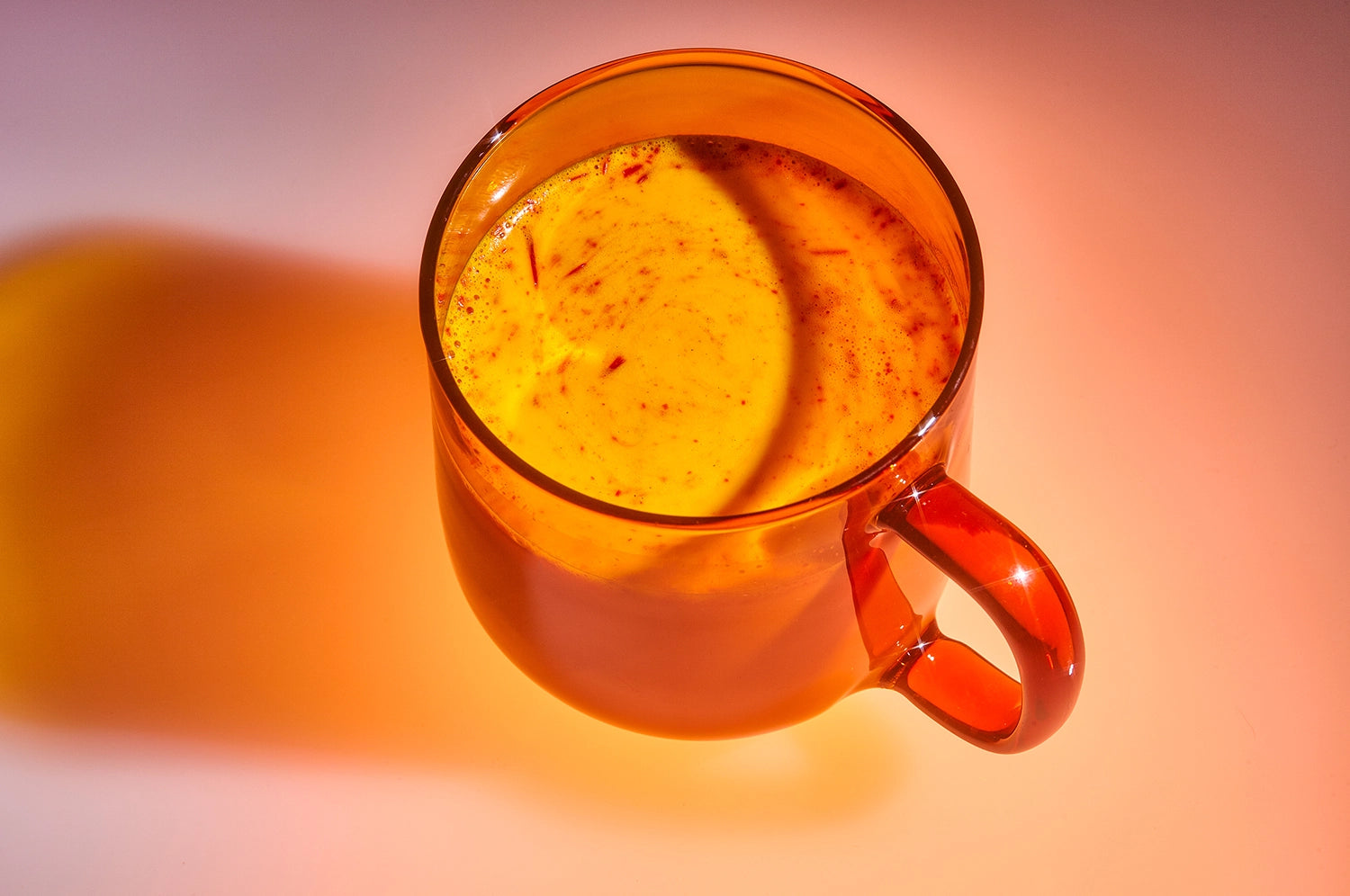 A clear orange hued mug filled with a golden-yellow saffron latte, enhanced with therapeutic-grade saffron from The Fullest, illuminated in warm light.