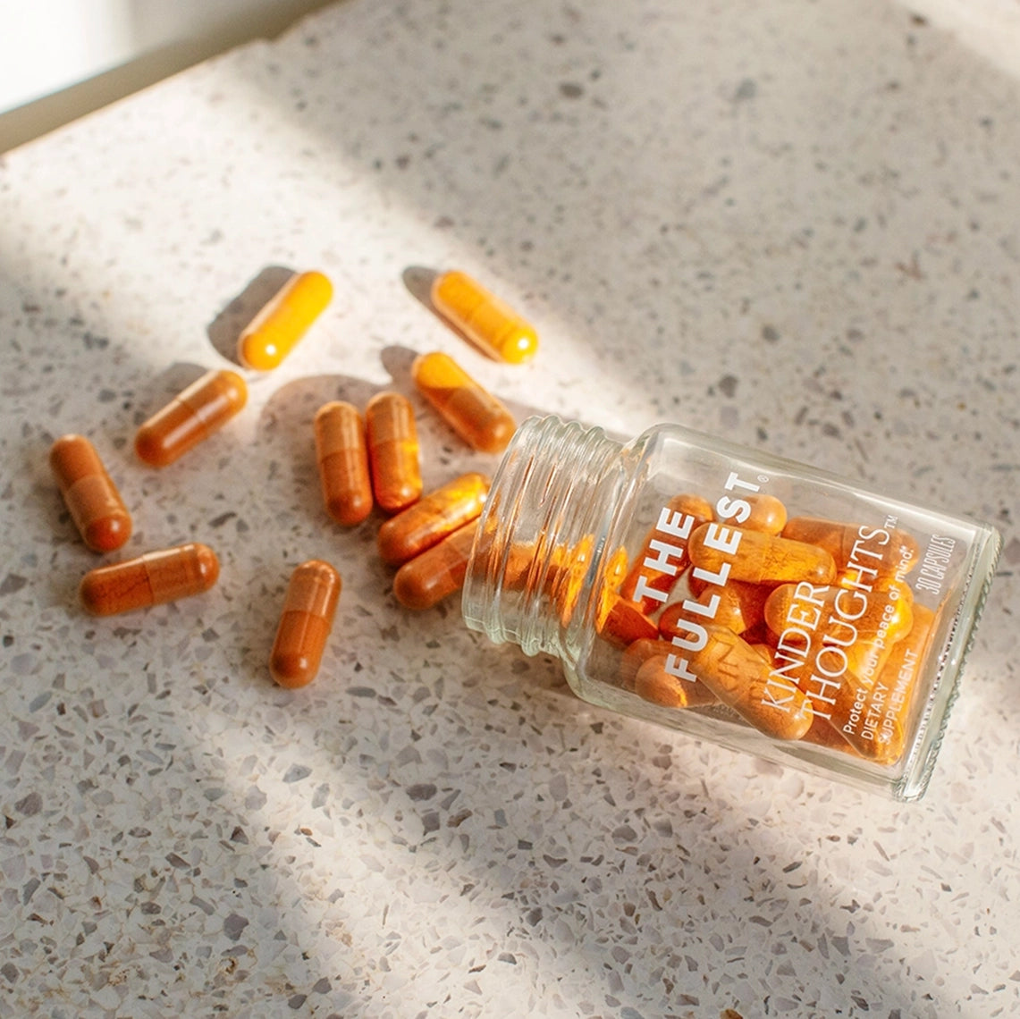 A bottle of orange saffron and turmeric capsules spilled on a sunlit counter, with capsules scattered around the open container.