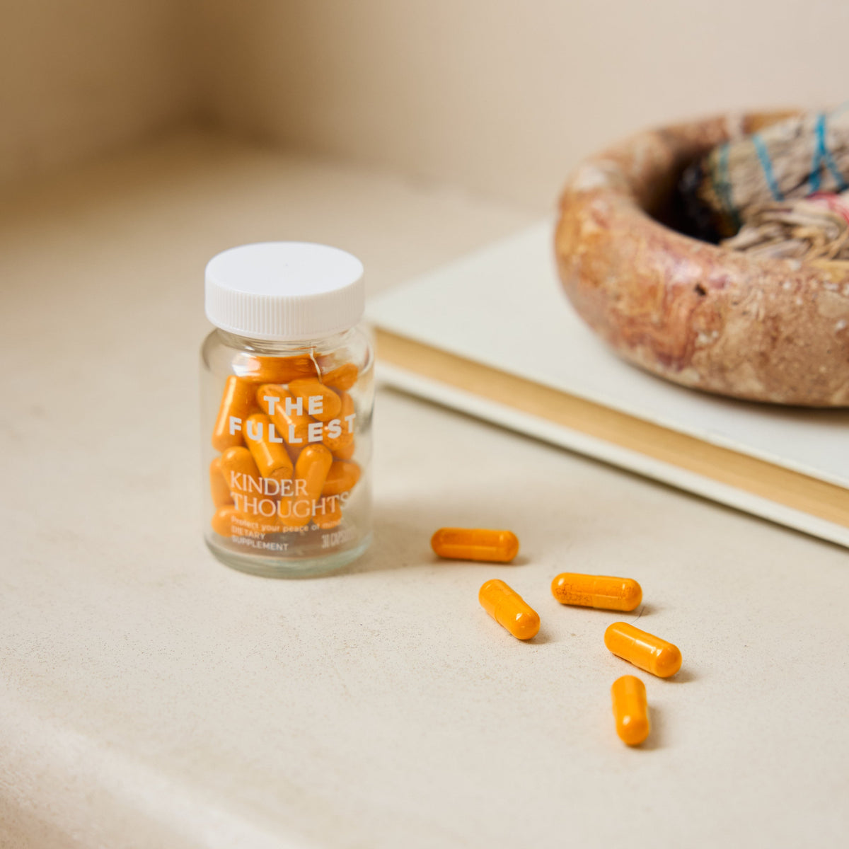 A clear jar labeled "THE FULLEST" Saffron Capsules sits on a beige surface, with six bright orange capsules scattered beside it.