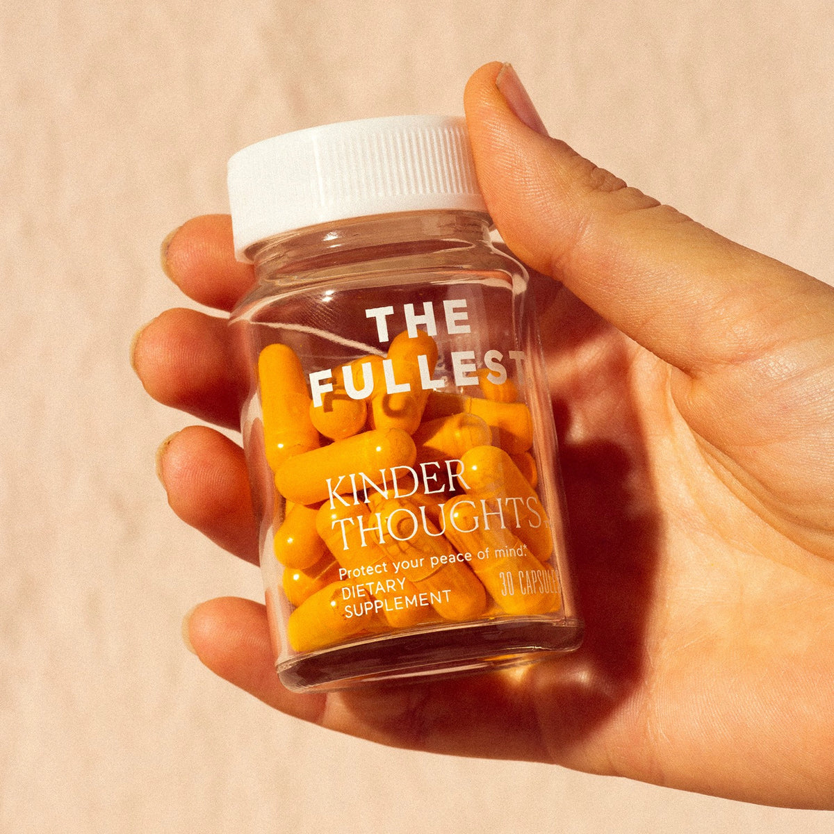 A hand holding a transparent bottle of Happy Habits Bundle supplements with the label &quot;THE FULLEST kinder thoughts&quot;.