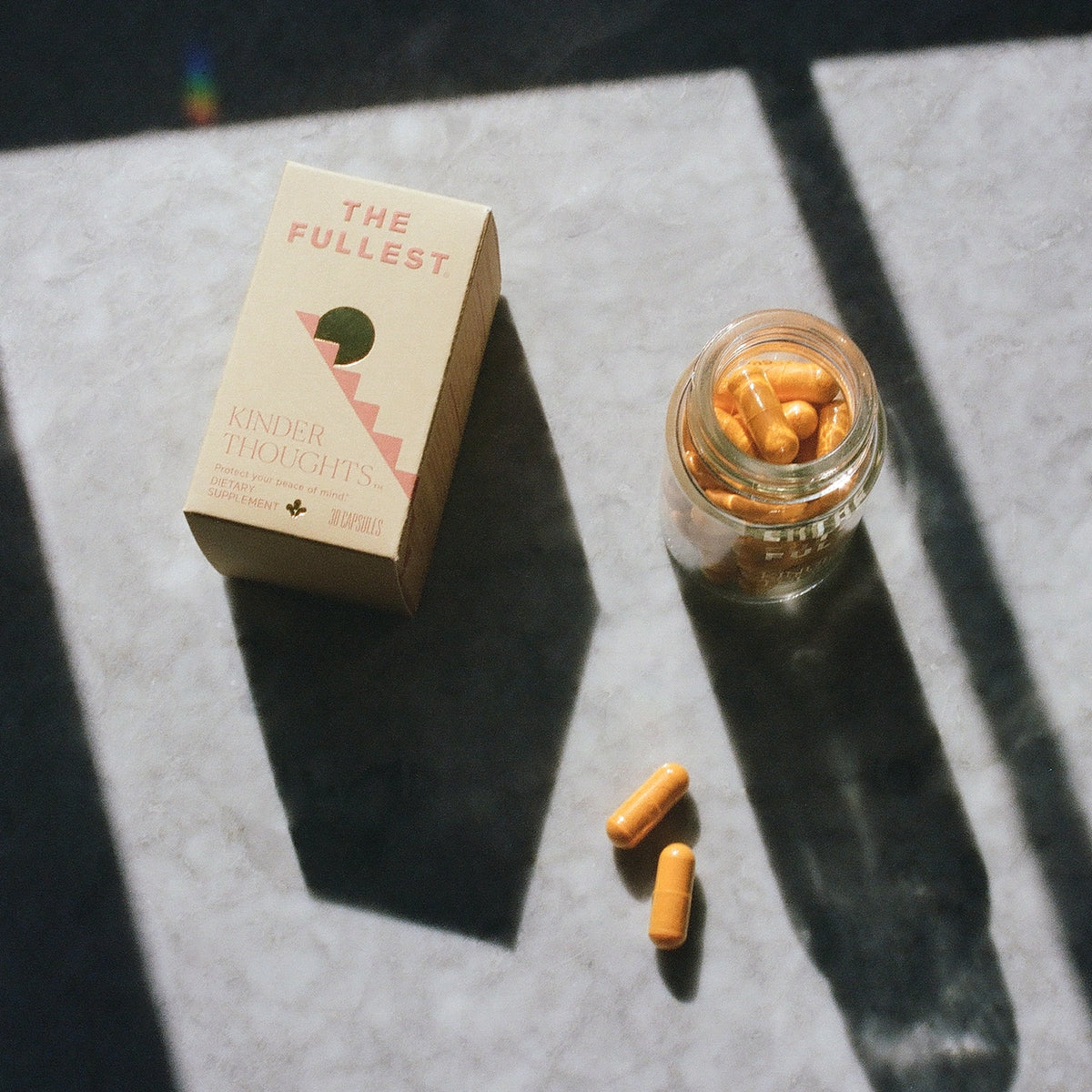 A box of &quot;Happy Habits Bundle&quot; saffron supplements beside an open glass jar with several capsules spilled out, in natural lighting with shadows.