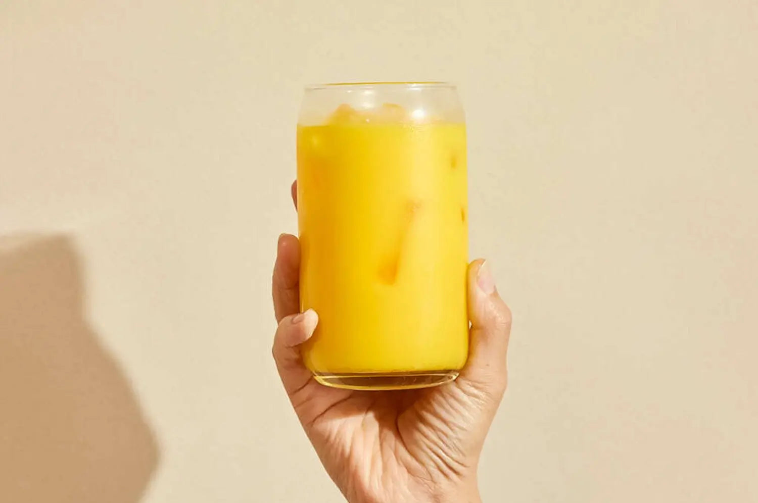 Iced Saffron latte in a clear tall glass in front of a beige wall