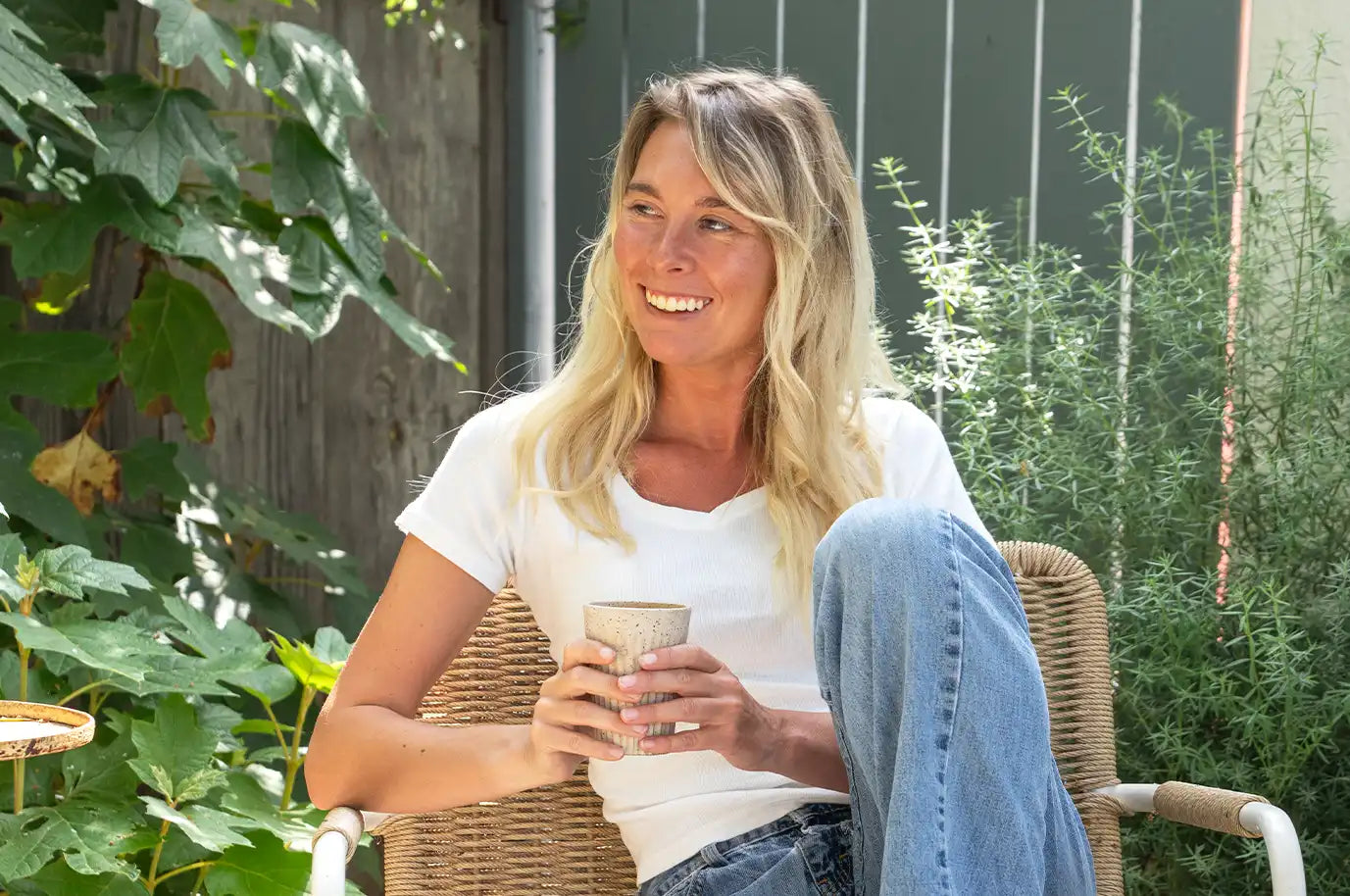 Woman smiling with ceramic mug in hand outside 