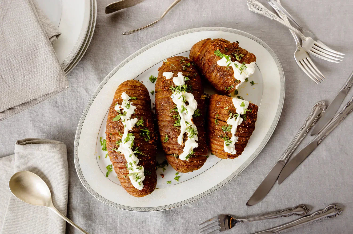Hasselback baked potatoes drizzled with saffron-infused butter using THE FULLEST’s Kinder Thoughts® capsules, topped with sour cream and fresh herbs, served on a white platter.