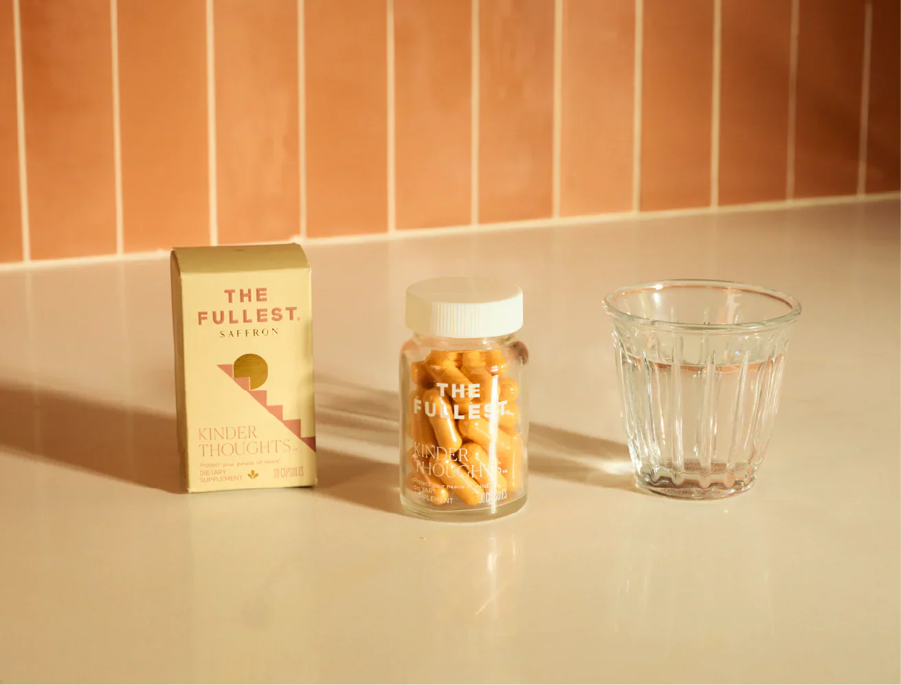 Photo of The Fullest Saffron Capsules on a counter top with orange tile background and glass of water