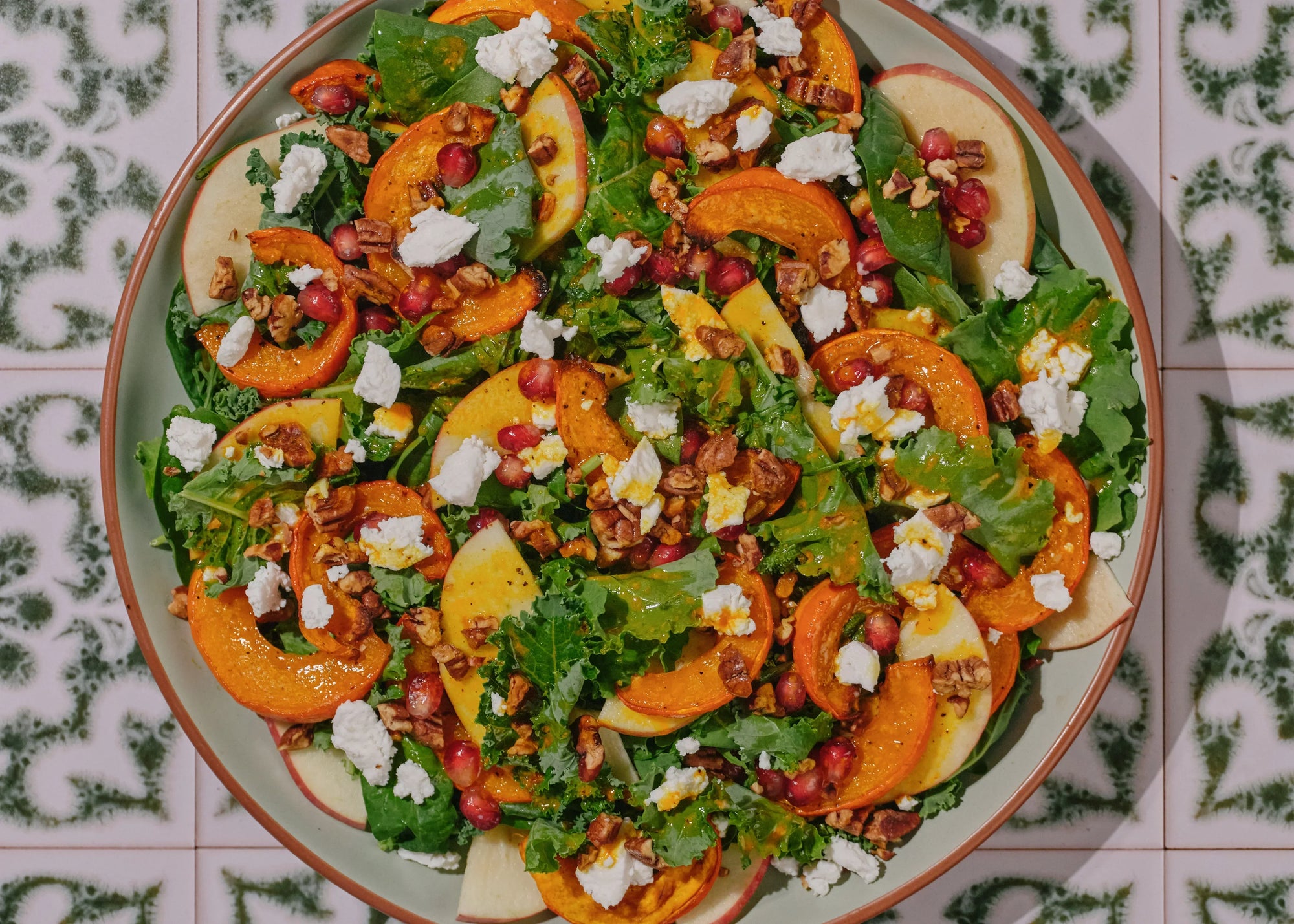 Fall harvest salad with mixed greens, kaboocha squash, pomegranate seeds & goat cheese in a bowl on top of a green counter top 