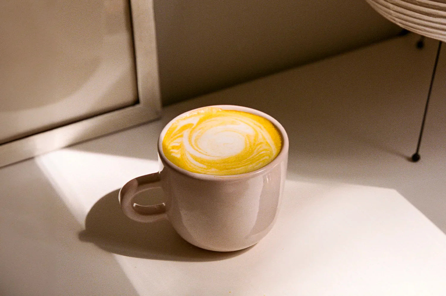 An image of a saffron latte made with The Fullest Saffronon Latte mix, served in a white mug on a countertop. 