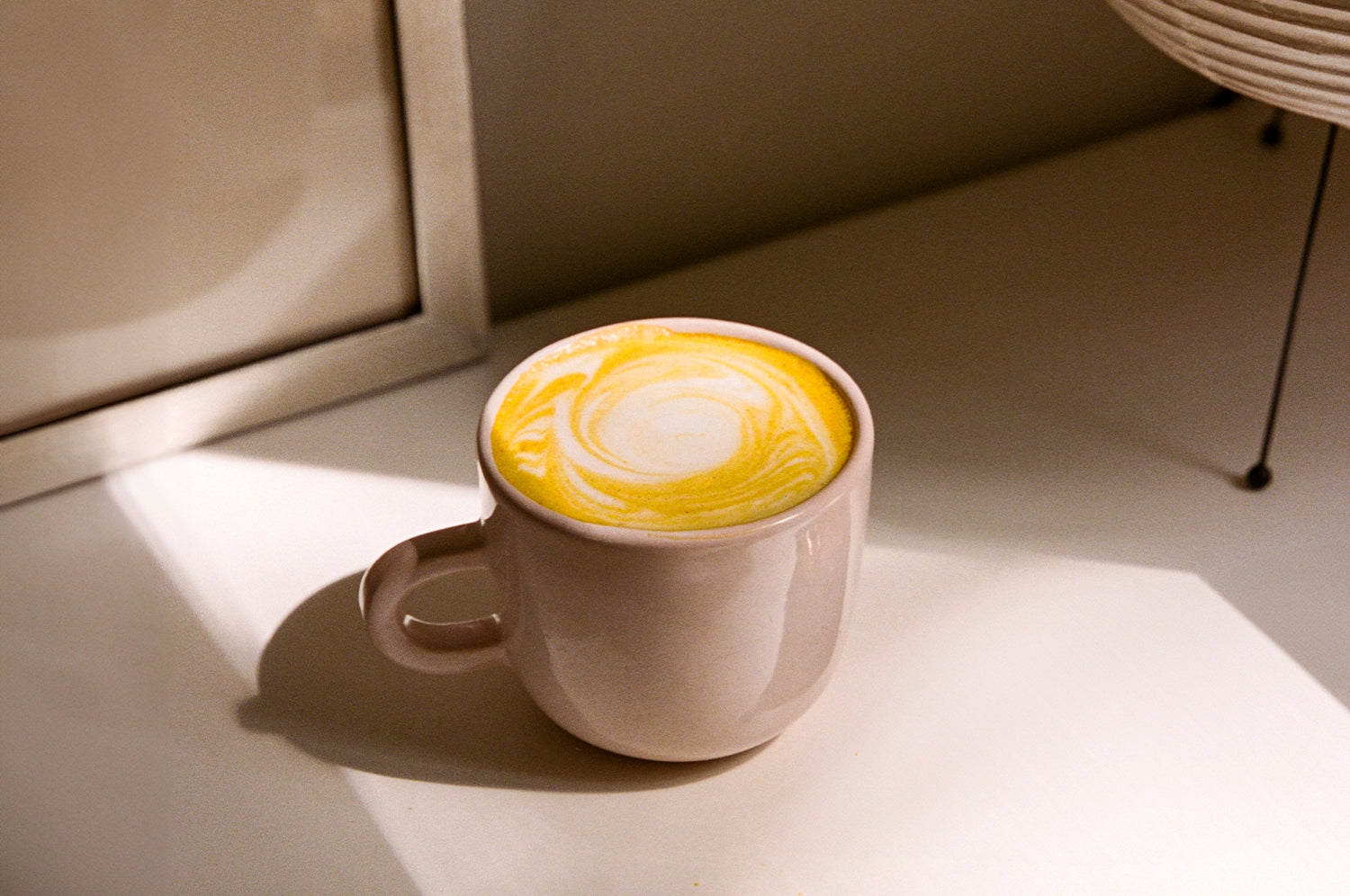 An image of a saffron latte made with The Fullest's Warm Feelings Saffron Latte mix, served in a white mug on a countertop. 