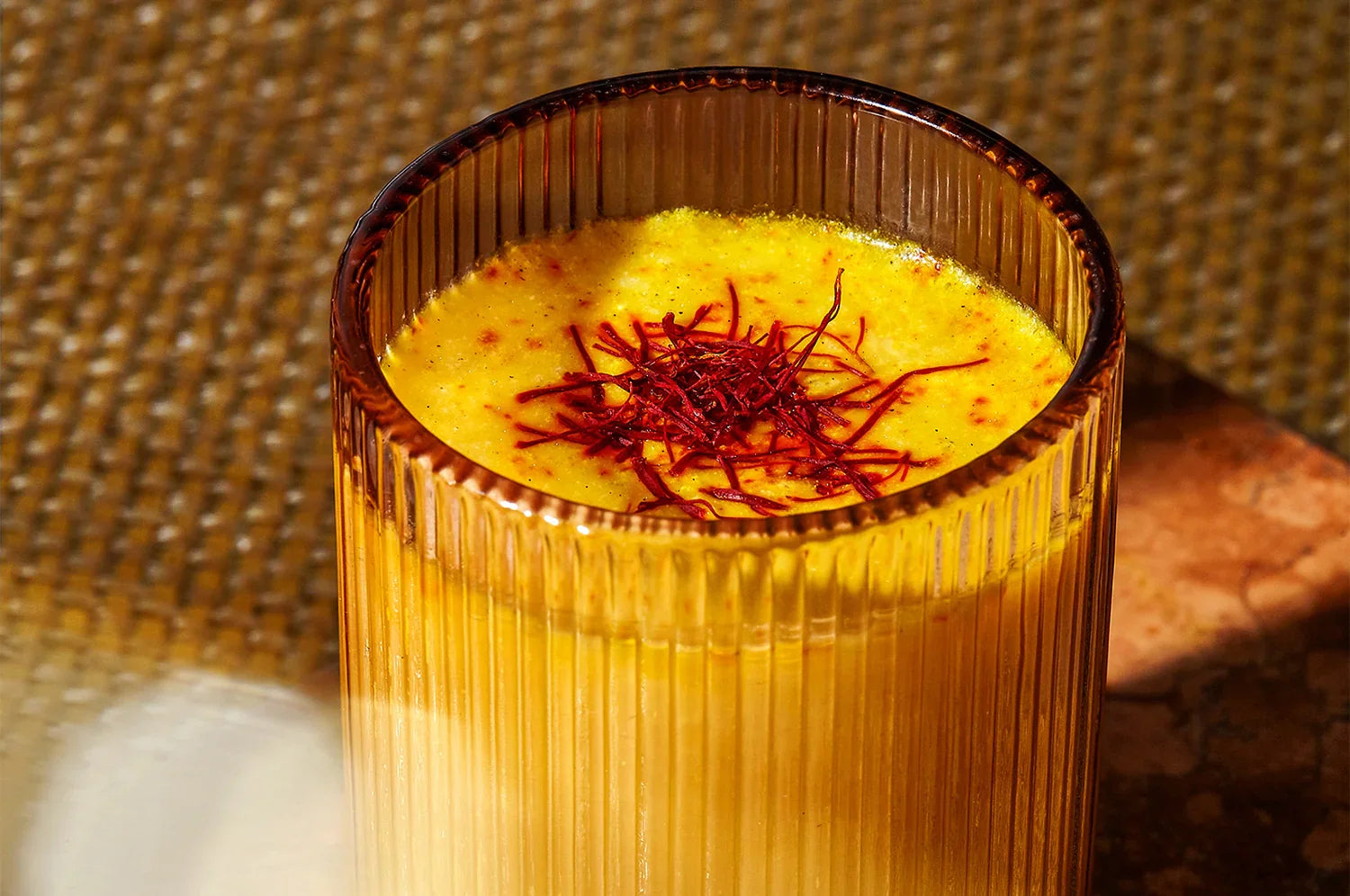 A glass of golden saffron-infused latte topped with The Fullest's saffron threads, placed on a textured surface.