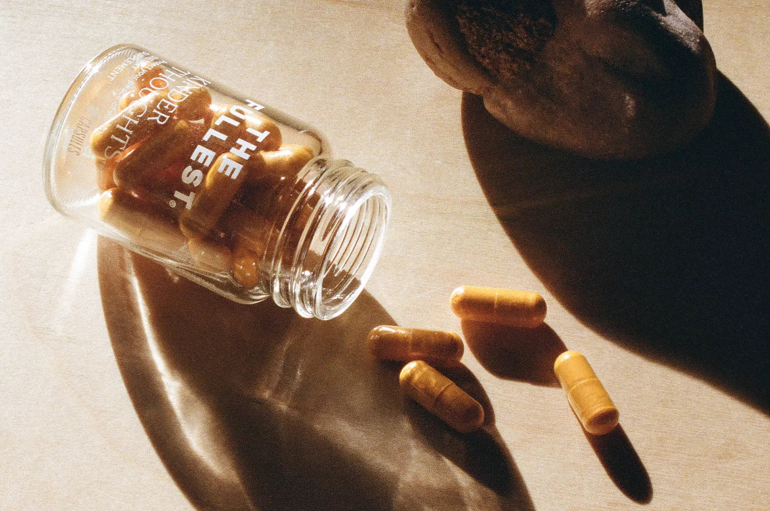 A bottle of The Fullest saffron and turmeric capsules spilled on a sunlit counter, with capsules scattered around the open container.