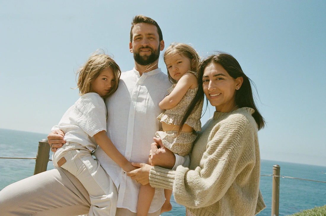 A heartwarming family portrait featuring Nikki Bostwick, founder and CEO of THE FULLEST, with her husband and two children, set against a serene ocean backdrop.