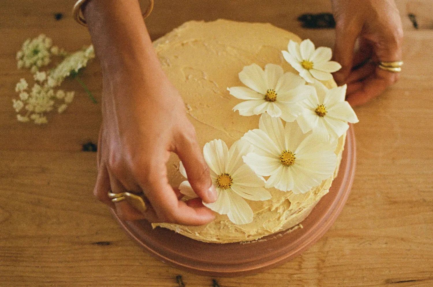 A woman placing flowers on top of an olive oil cake adorned with mood-boosting saffron buttercream frosting from The Fullest.