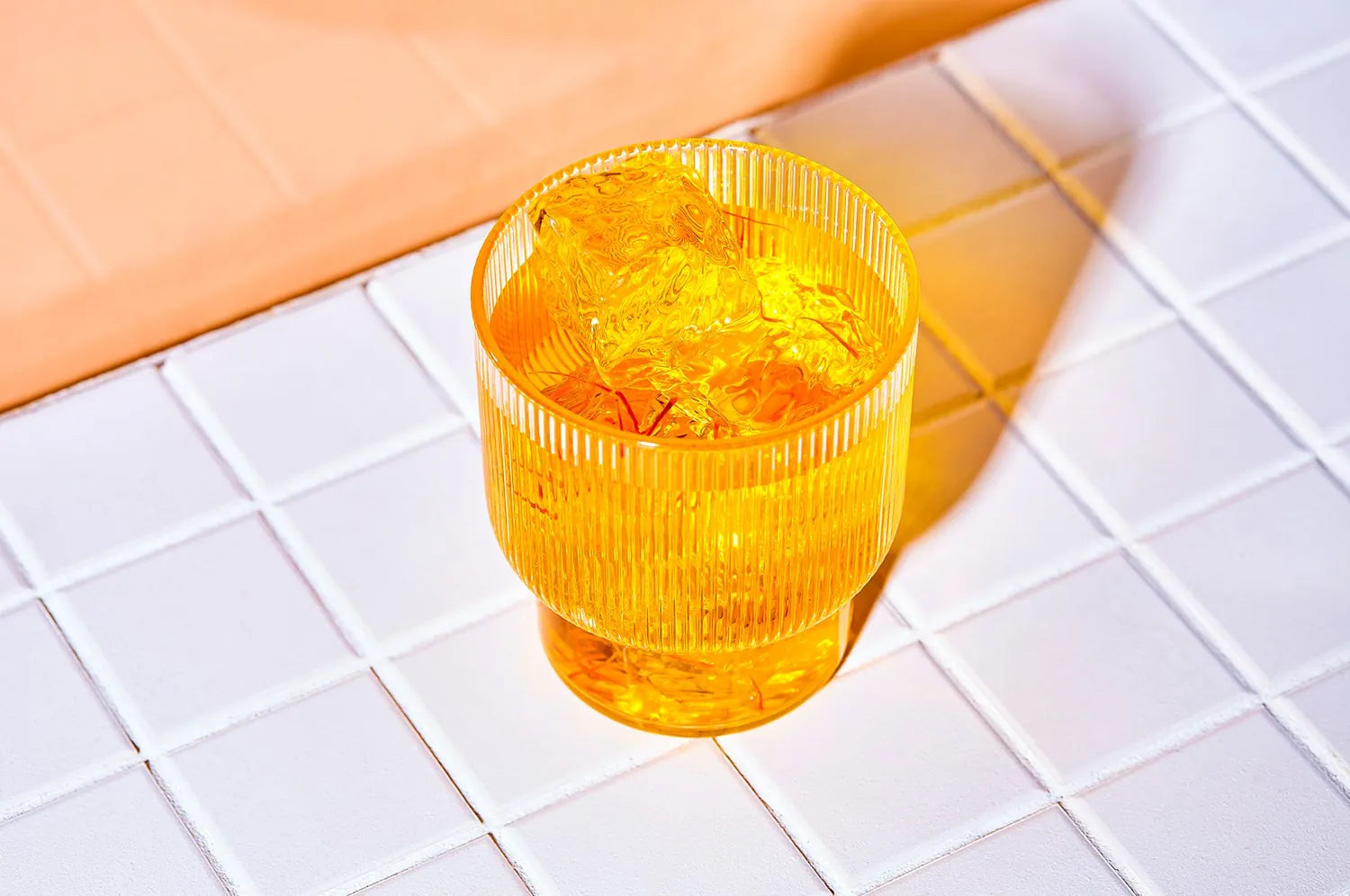 A glass of saffron tea over ice sitting on a white countertop.