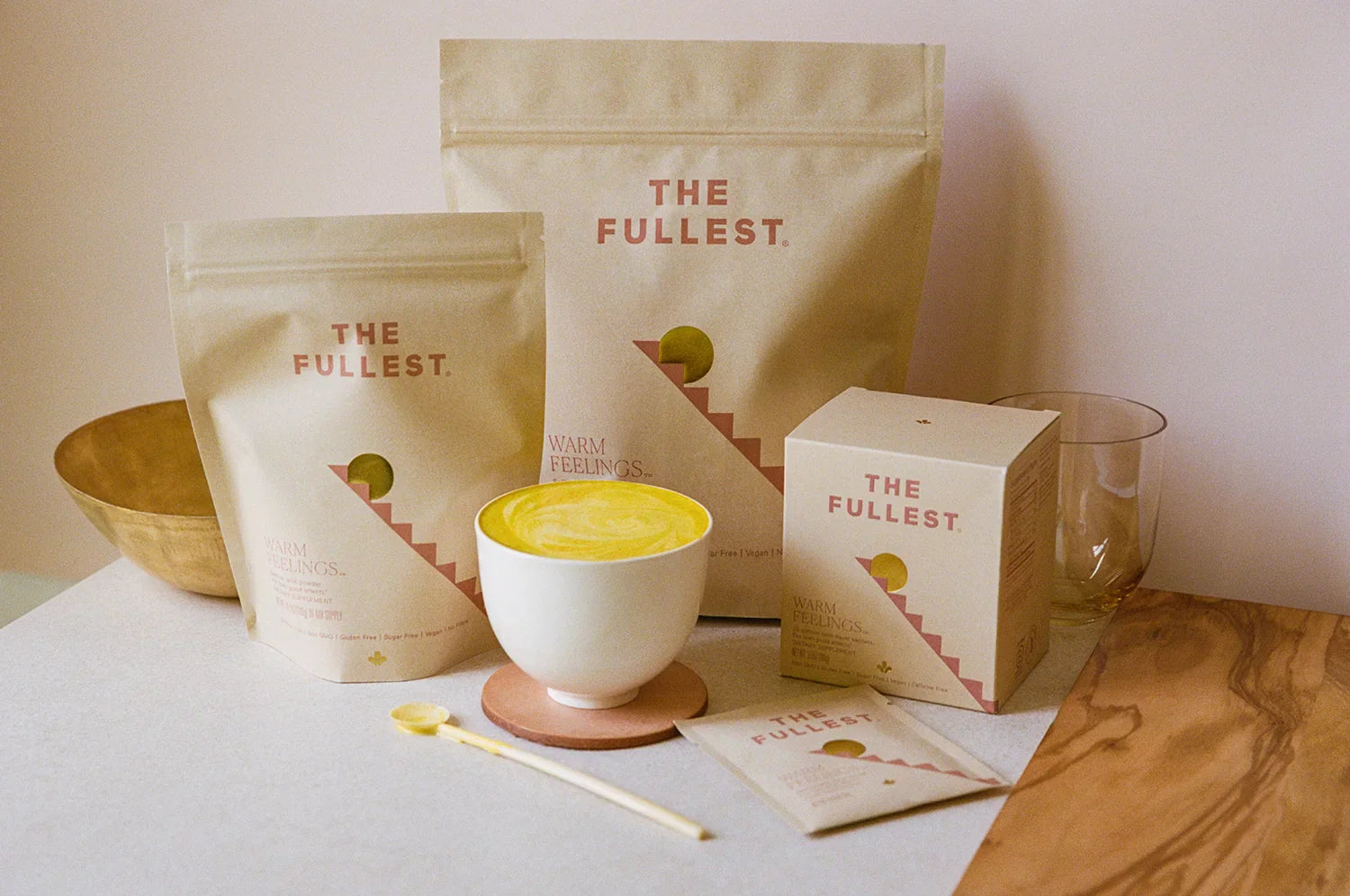 THE FULLEST Saffron Latte powder in bulk, bag, and sachets sizes standing on a countertop alongside a cup of the Warm Feelings saffron latte.