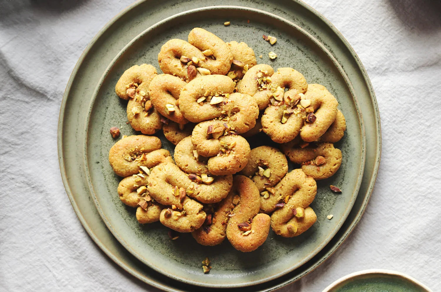 A plate of homemade saffron cookies using the Warm Feelings Saffron Latte mix topped with chopped nuts, viewed from above on a light fabric surface.