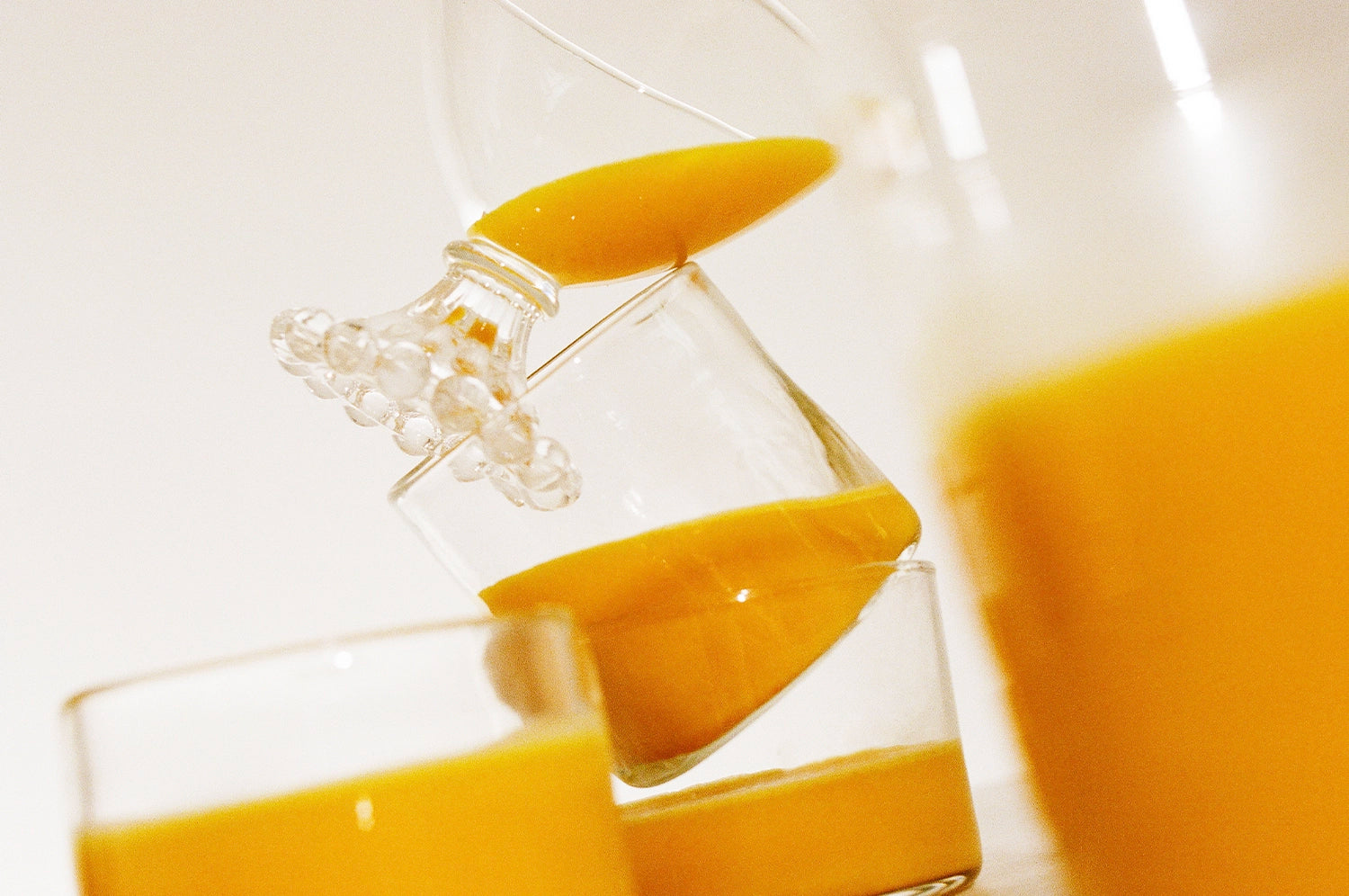 A close-up of orange saffron beverage from The Fullest being poured from a glass jug into a glass, with another full glass visible in the foreground.