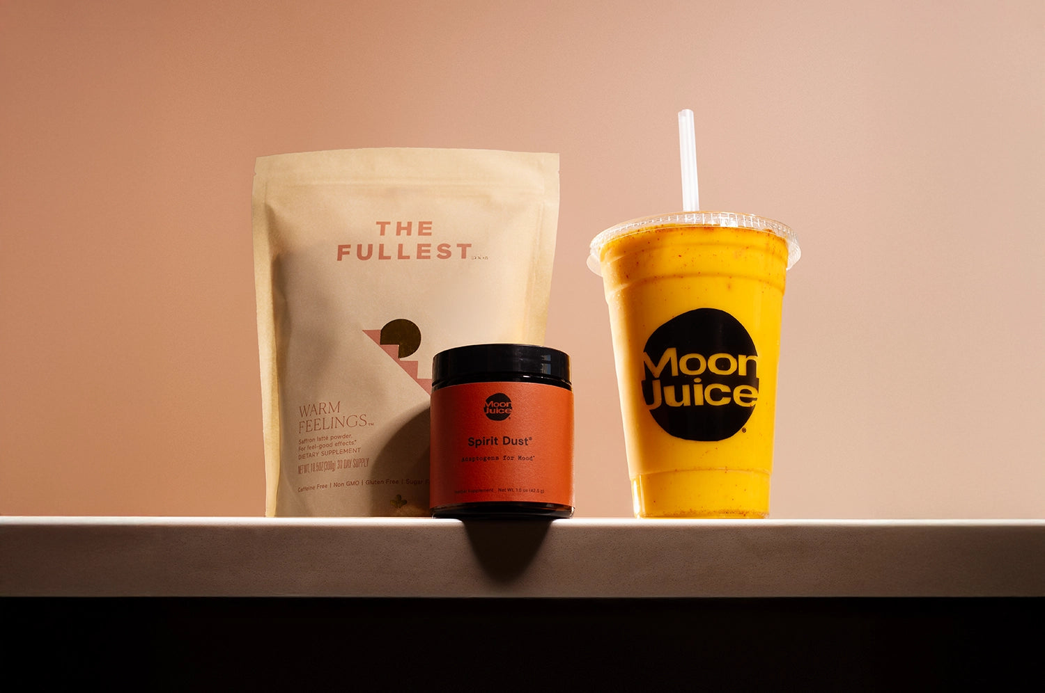 Spirit Saffron Latte collaboration between THE FULLEST and Moon Juice, featuring Warm Feelings® saffron latte powder, Spirit Dust jar, and a vibrant yellow latte in a Moon Juice cup.