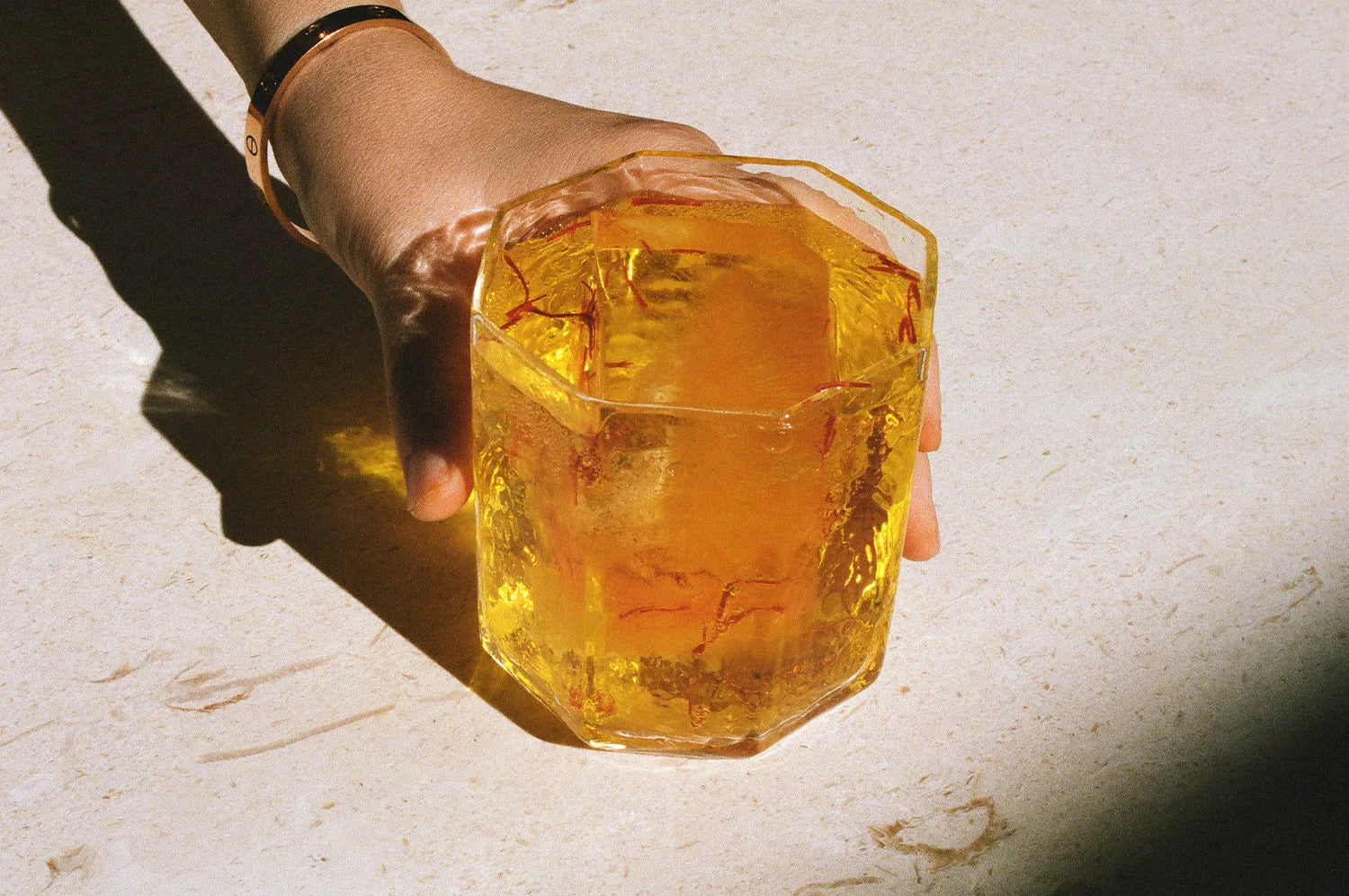A model poses with a glass of saffron tea from The Fullest, placed on a white counter.