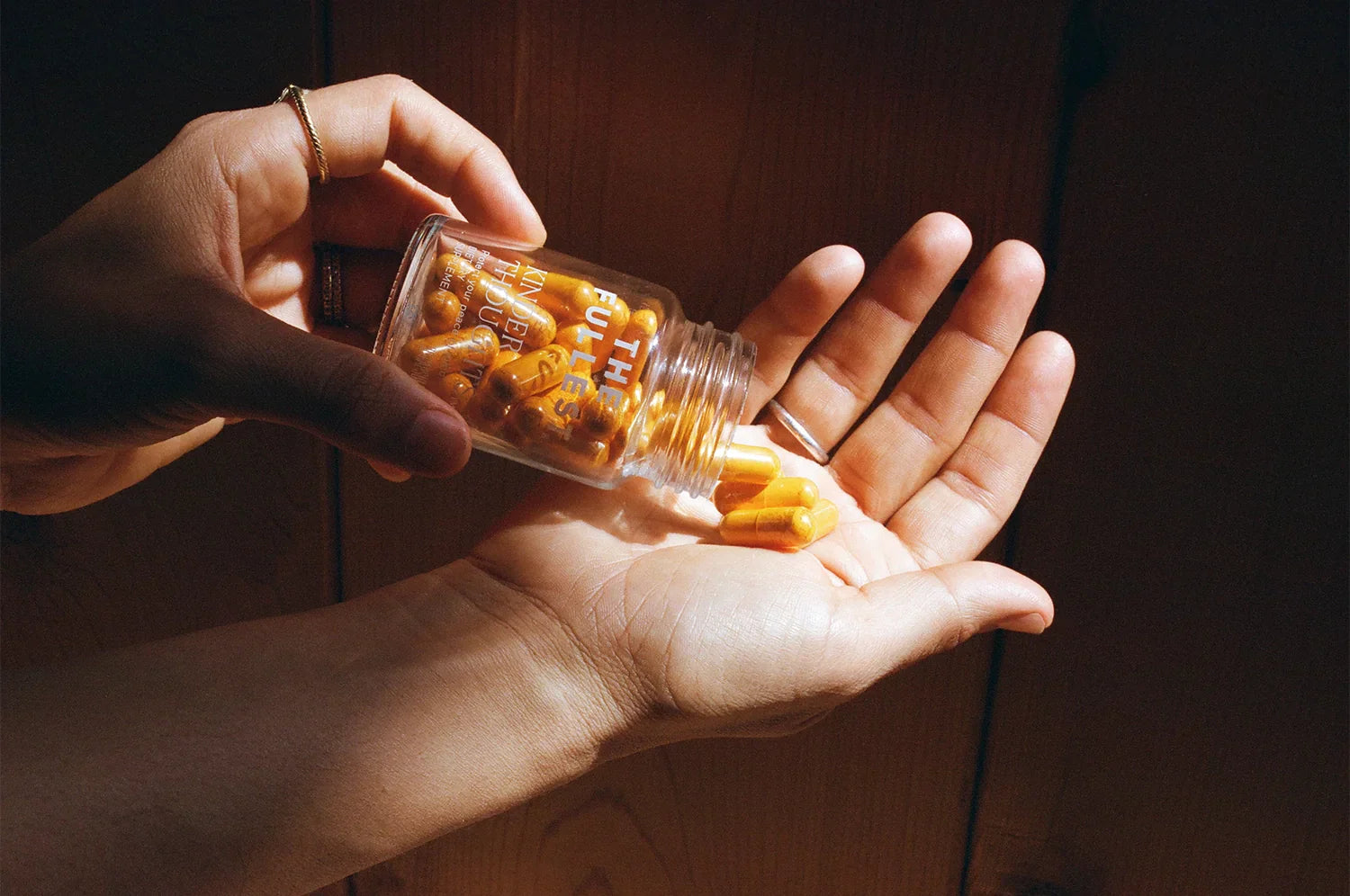 A close-up image shows a hand holding a small glass jar of saffron capsules labeled “THE FULLEST KINDER THOUGHTS” as another hand tilts the jar, allowing the capsules to spill gently into the palm.
