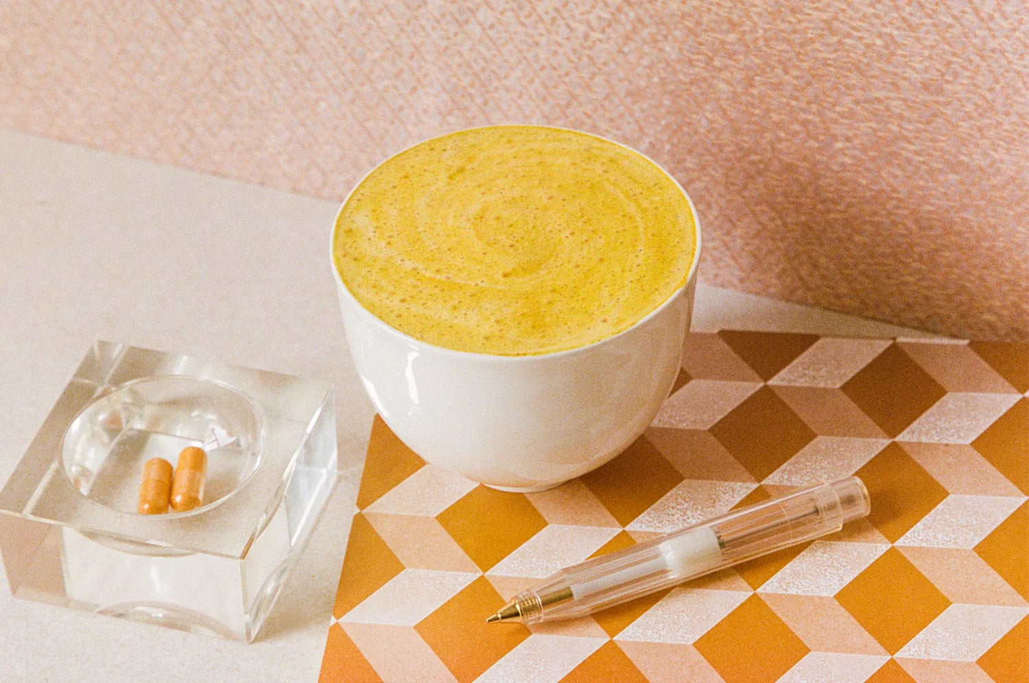 An image of a saffron latte in a white mug beside a glass tray holding two saffron capsules by THE FULLEST.