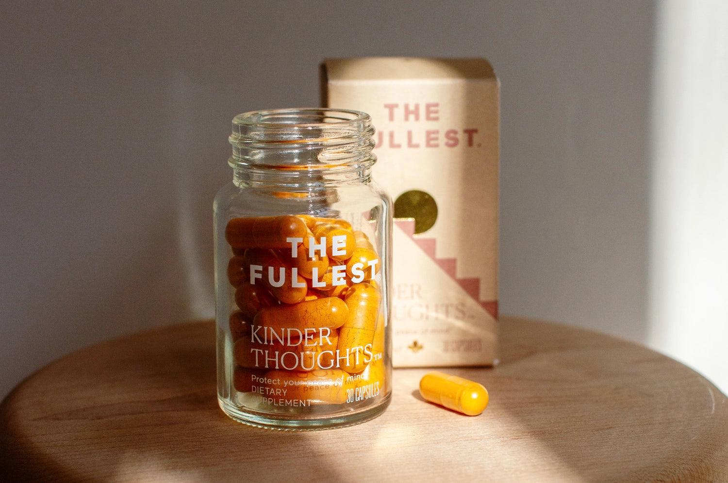 A bottle of THE FULLEST Kinder Thoughts saffron and turmeric supplement, with the lid off and placed next to its branded box.