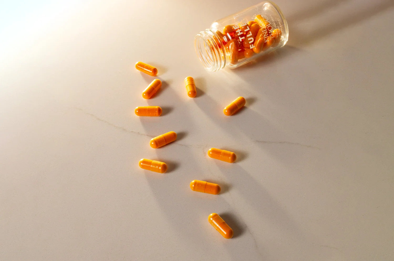 A bottle of THE FULLEST's Kinder Thoughts saffron capsules spilled out onto a marble countertop.