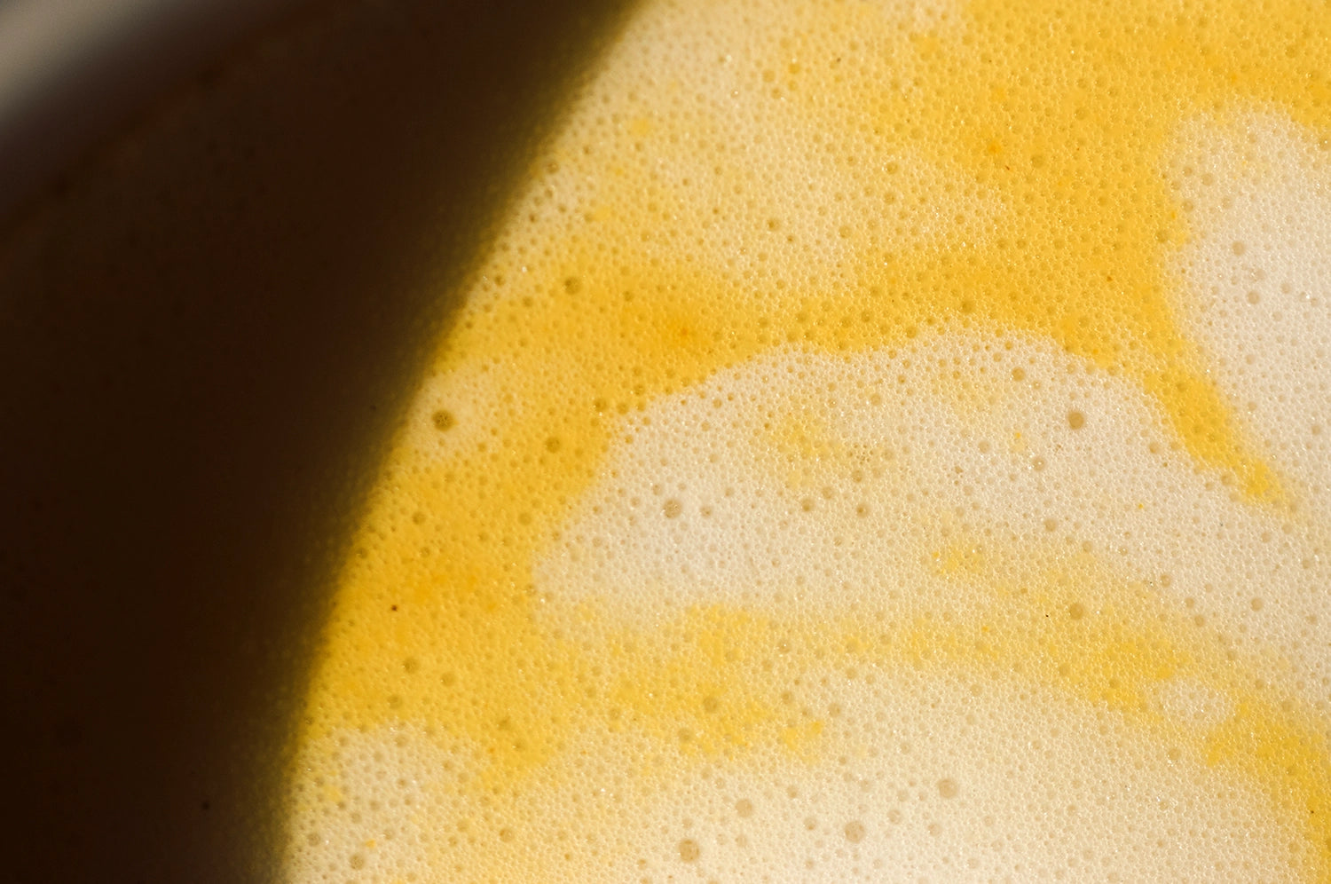 A close up photograph of a cup of THE FULLEST's Warm Feelings saffron latte prepared with frothy milk in direct sunlight. 