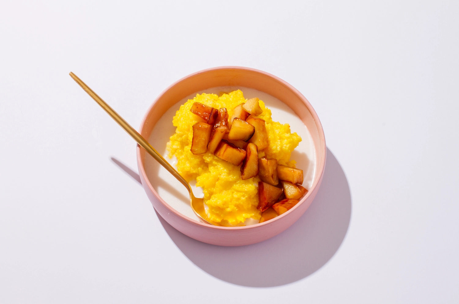 A bowl of THE FULLEST's saffron coconut congee topped with stewed fruit against a white background.