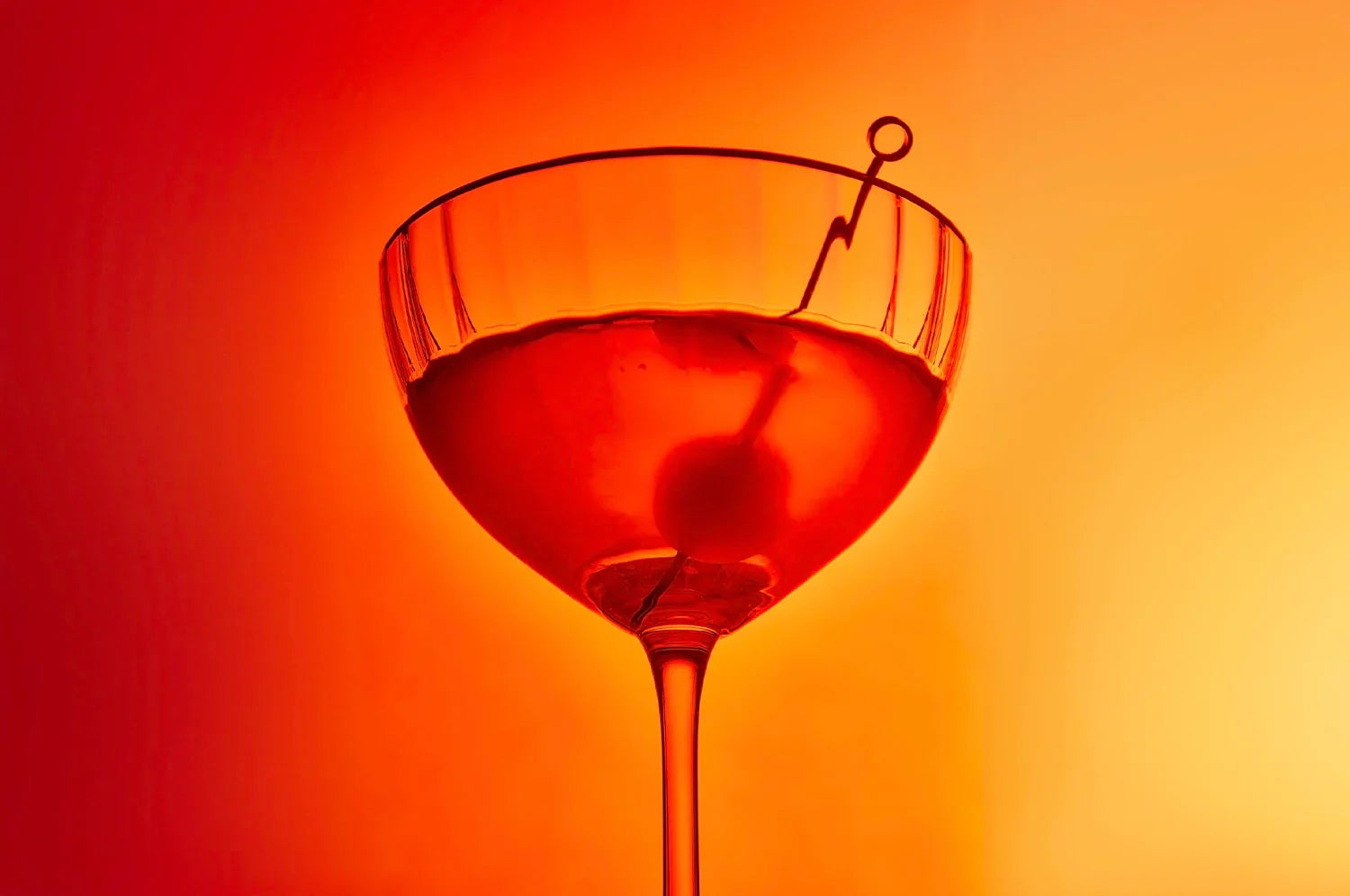 A cocktail glass filled with SLOWDAYS Saffron Spritz with THE FULLEST's Warm Feelings saffron latte powder against an orange background.