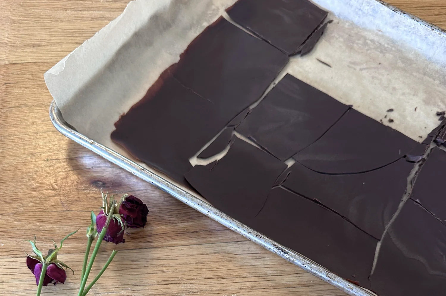 A baking sheet lined with parchment paper holds dark Saffron Cacao Honey Bars cut into squares. Beside the bars are dried roses, adding a natural touch. Made with THE FULLEST’s Warm Feelings® saffron latte blend.