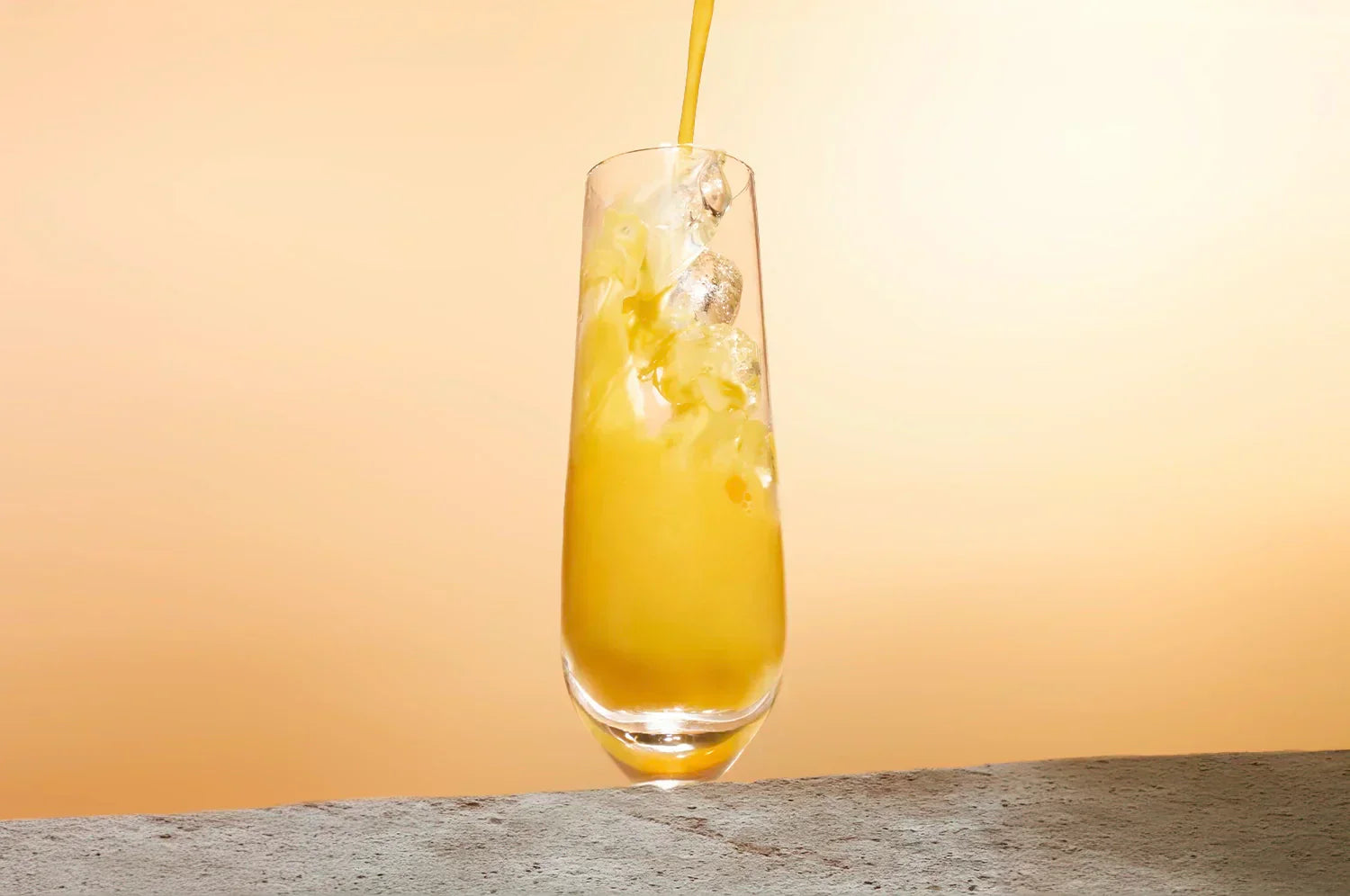 THE FULLEST Saffron Latte being poured into a tall glass of ice against an orange background.