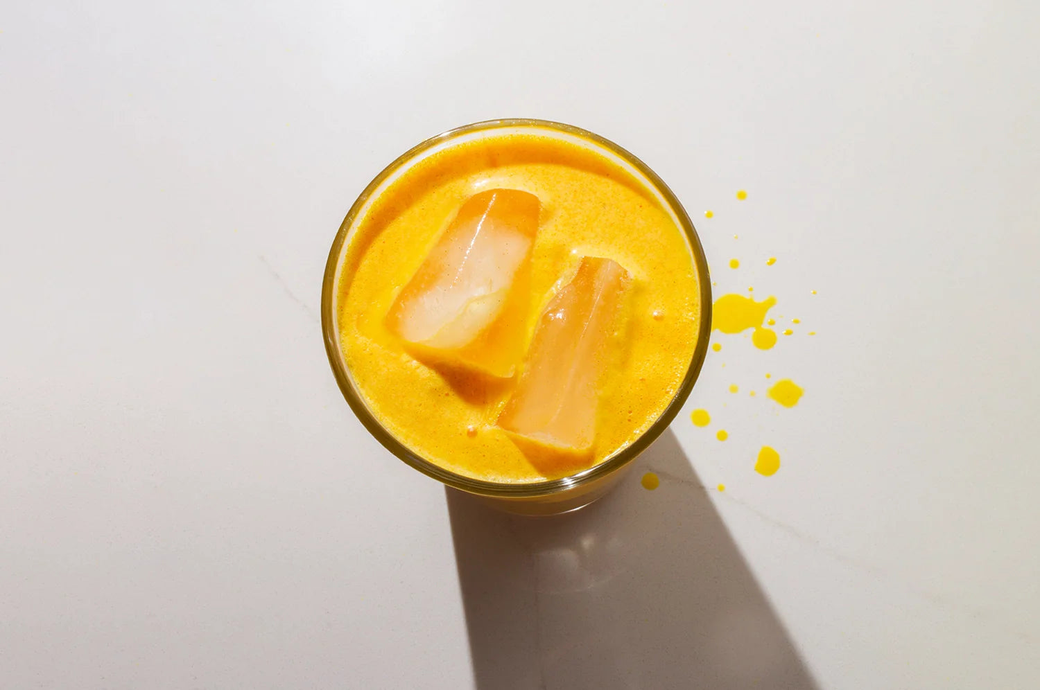 A cup of THE FULLEST's Warm Feelings saffron latte on ice on a light marble surface.