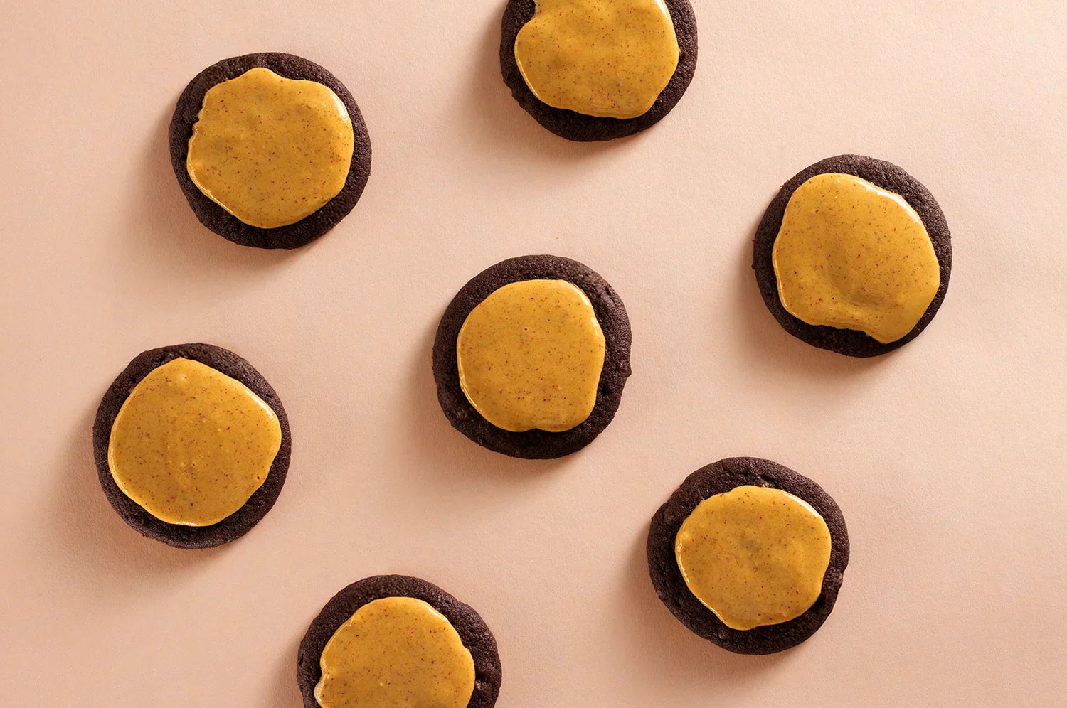 Halloween-themed Charcoal Cookies topped with saffron frosting arranged on a light beige background. The dark, activated charcoal cookies contrast with the golden saffron frosting.