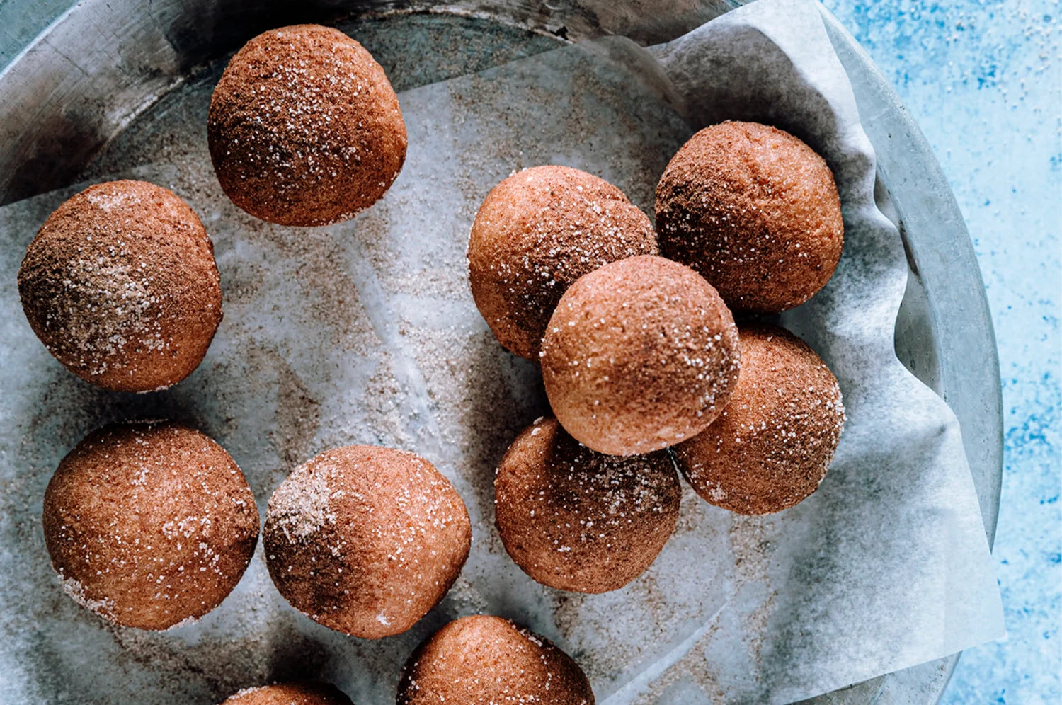 THE FULLEST's High Protein Warm Feelings Saffron Bites resting on a parchment-lined metal tray, lightly dusted with cinnamon and sugar. The round bites have a soft texture and a warm golden-brown hue.
