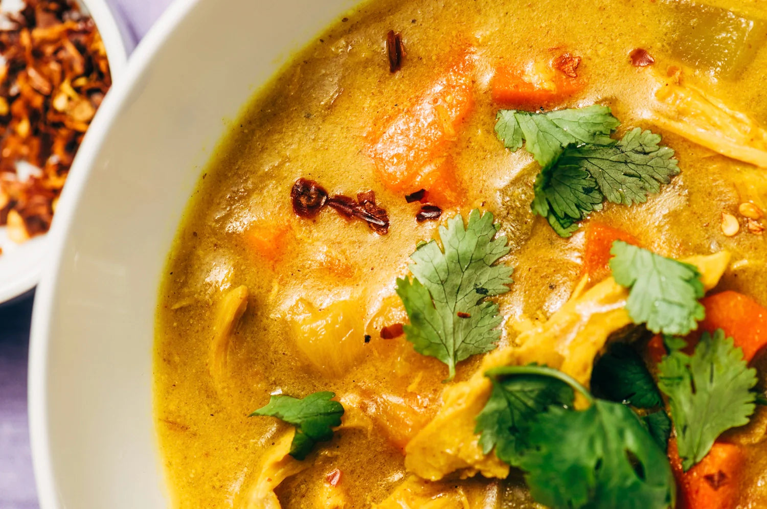 Close-up of a warm saffron chicken soup featuring tender chicken pieces, sliced carrots, celery, and noodles in a golden broth infused with Kinder Thoughts saffron capsules for added health benefits.