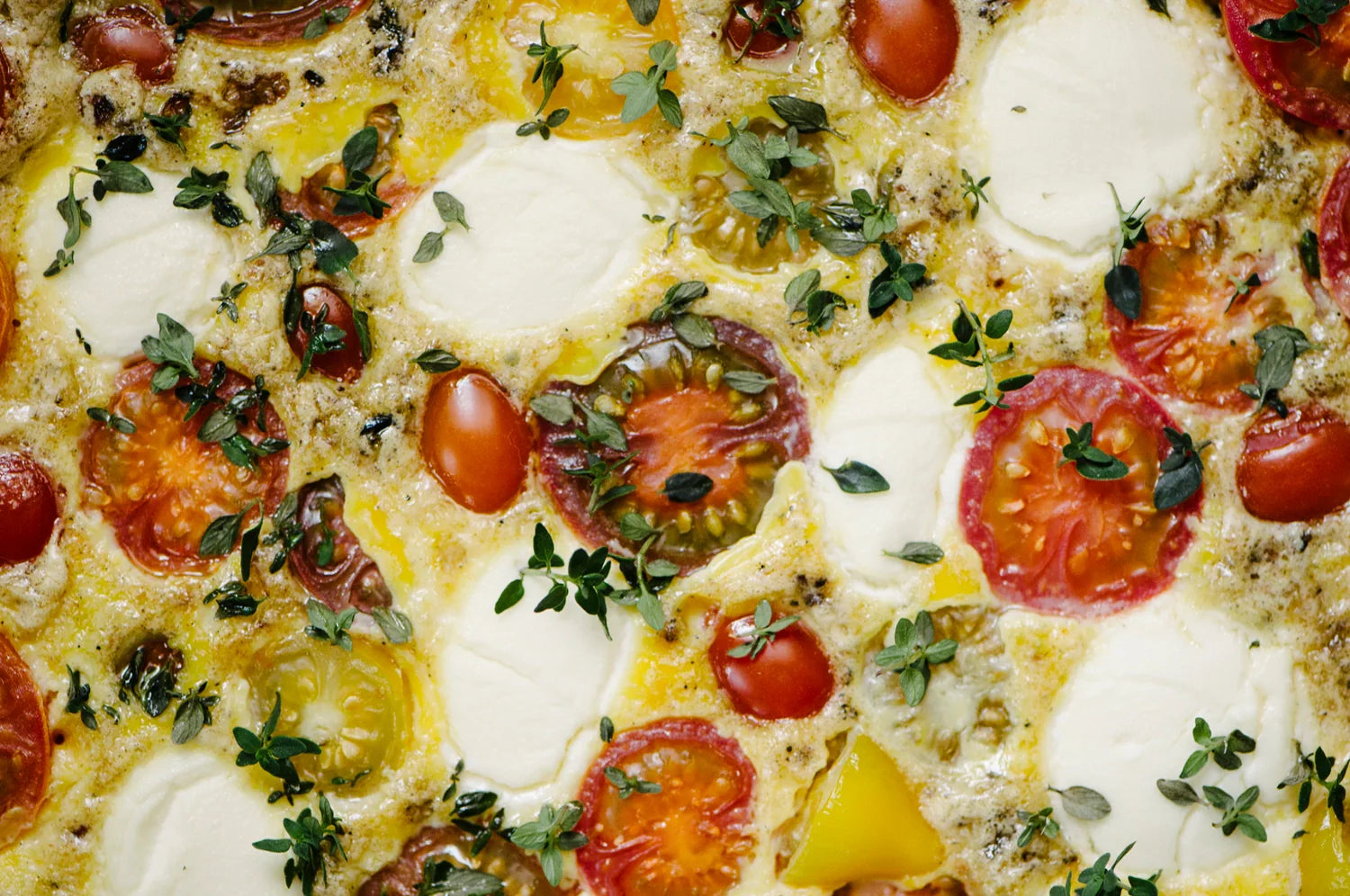 Close-up of THE FULLEST’s Kinder Thoughts® saffron frittata, topped with vibrant cherry tomatoes, creamy cheese, and fresh thyme.