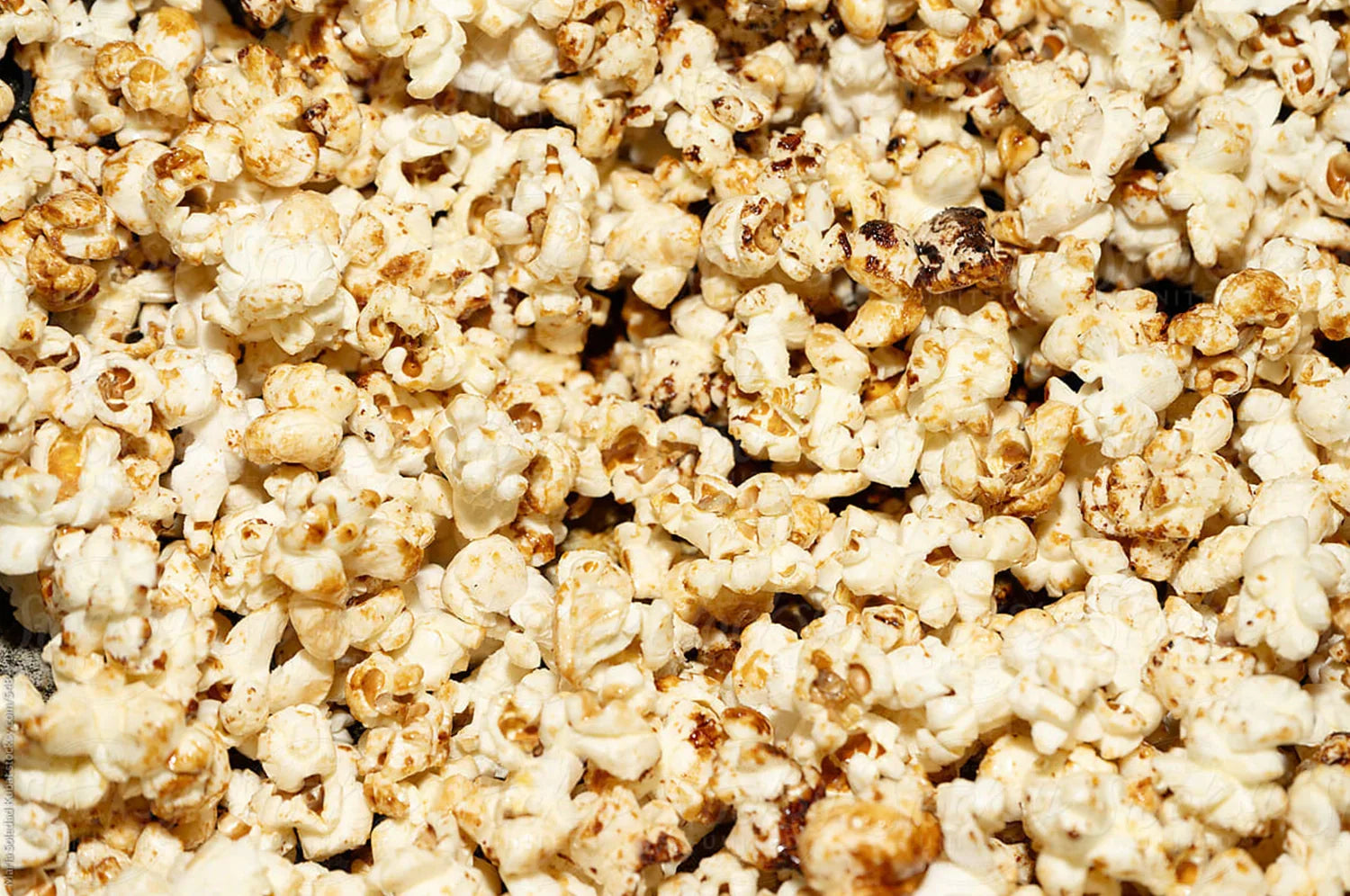 A close-up of freshly popped saffron buttered popcorn, glistening with melted grass-fed organic butter and sprinkled with the vibrant contents of THE FULLEST’s Kinder Thoughts® saffron capsules. 