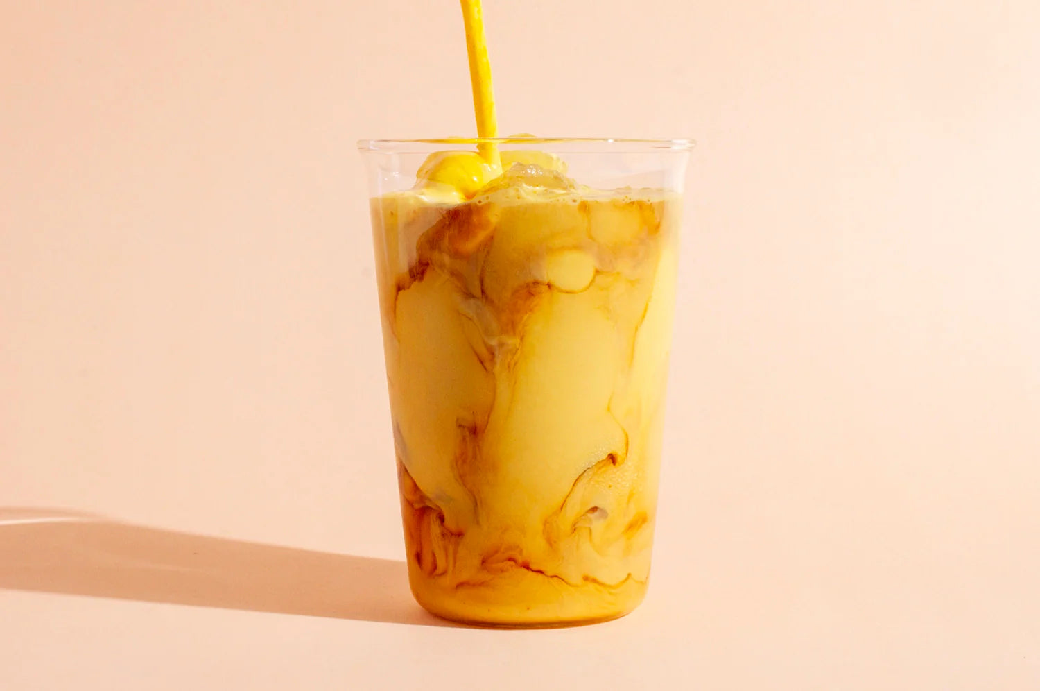 A cup of iced coffee with THE FULLEST's Warm Feelings saffron latte being poured into it.