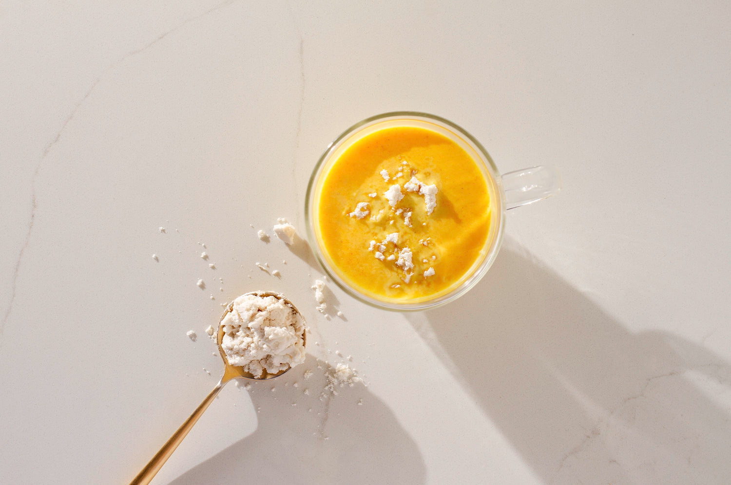 A cup of THE FULLEST's Warm Feelings Saffron Latte next to a spoonful of Keto Brainz Creamer 