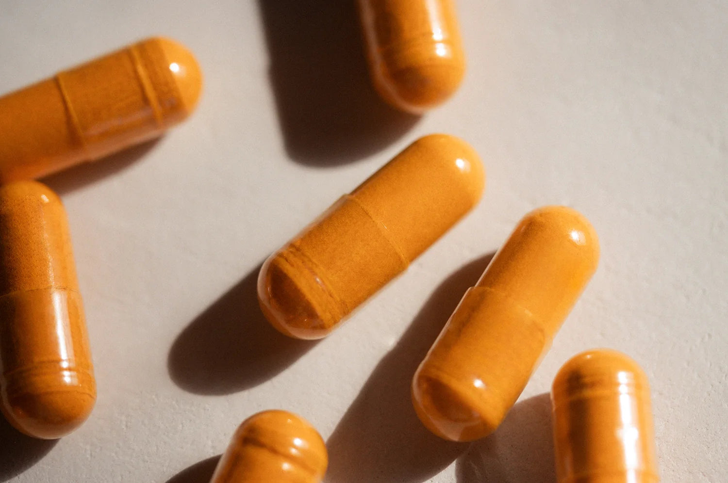 A bunch of THE FULLEST's Kinder Thoughts saffron capsules laid out on a beige surface in direct light.