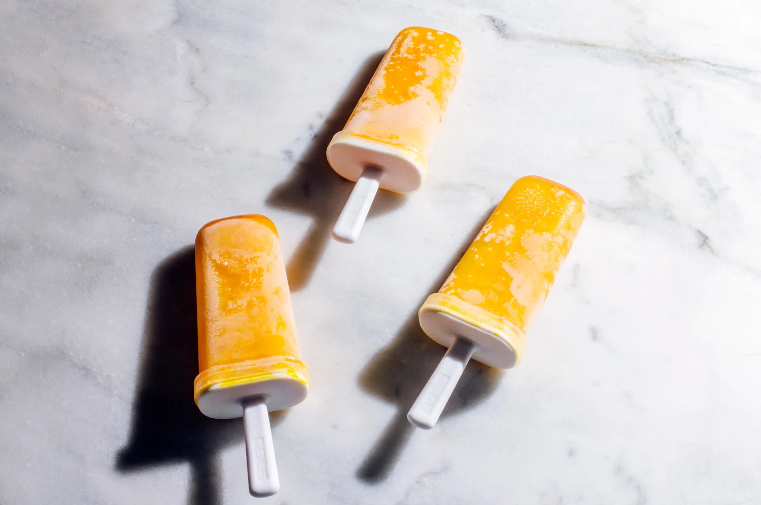 Three vibrant saffron, date, and lime popsicles resting on a granite countertop.