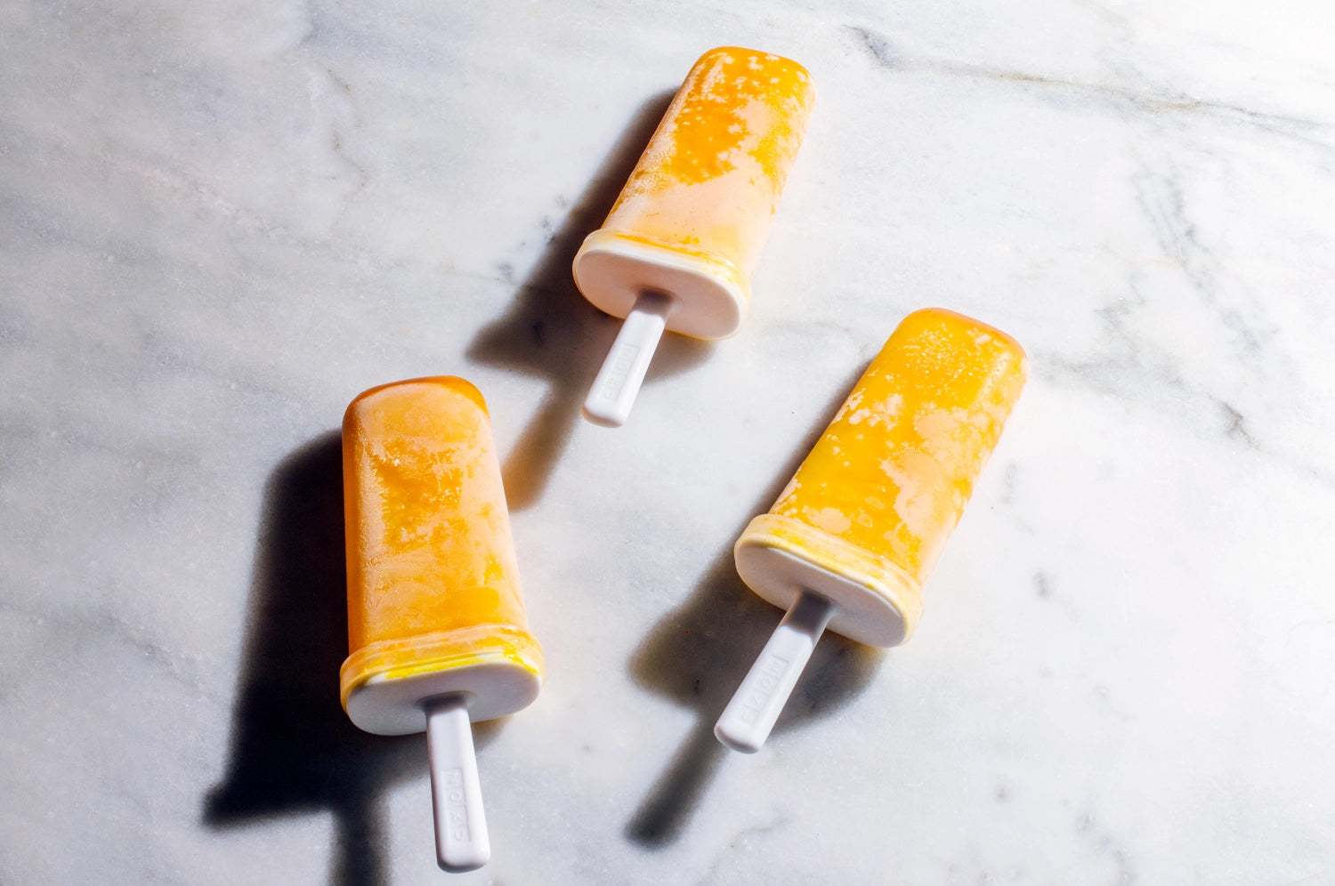 Three vibrant saffron, date, and lime popsicles resting on a granite countertop.