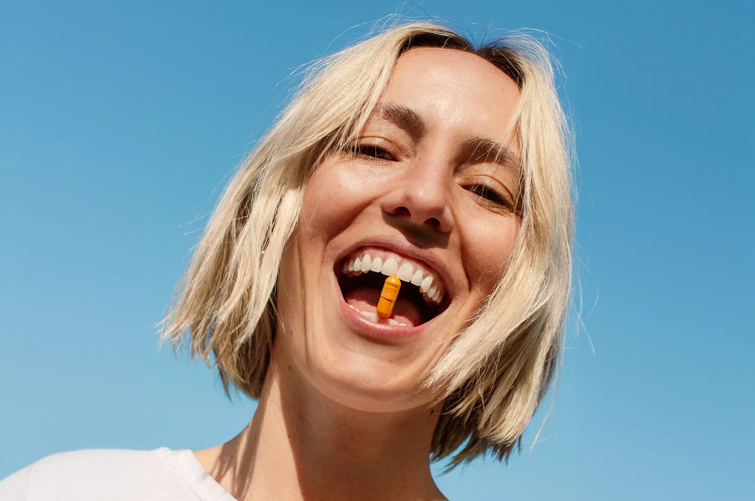A woman with a short blonde bob with a Kinder Thoughts saffron capsule being held between her mouth.