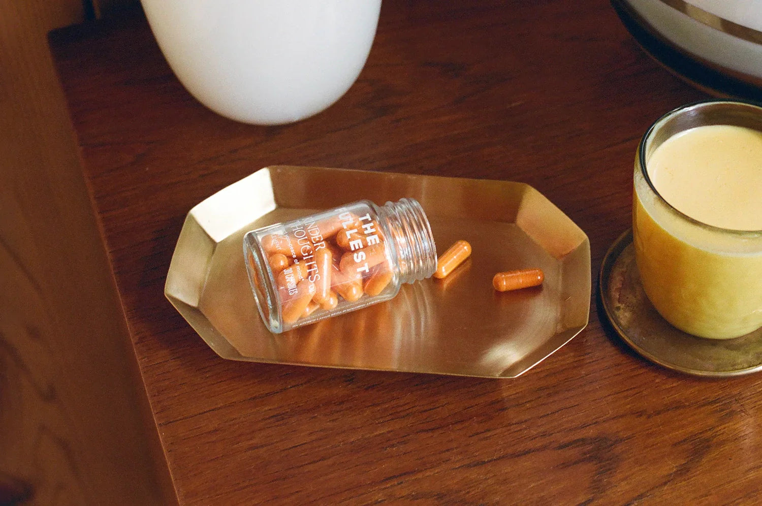 Kinder Thoughts saffron capsules resting on a brass tray, showcasing their elegant glass packaging and the saffron’s natural benefits, alongside a warm latte in the background.