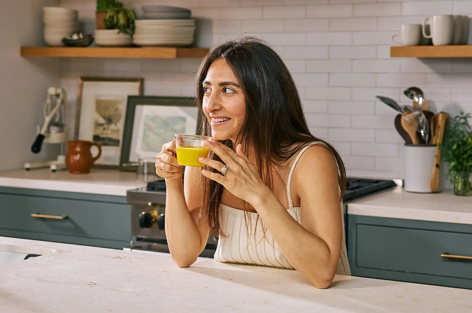 Founder Nikki Bostwick sipping on saffron latte leaning on granite counter 