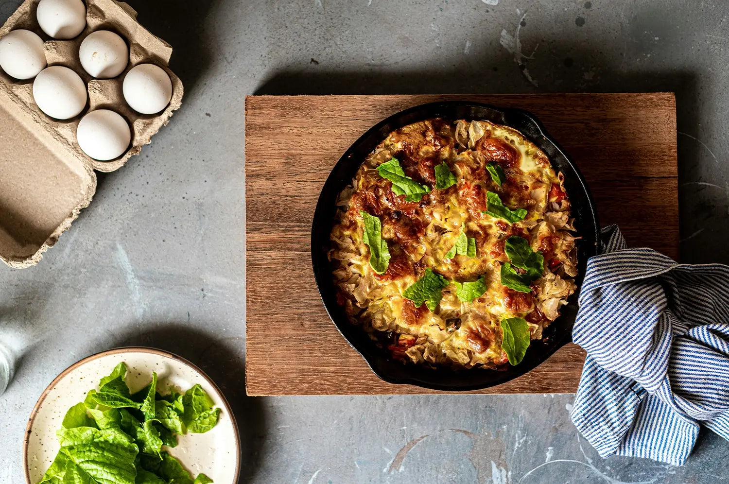 Rustic egg frittata in a cast iron skillet, topped with fresh greens and surrounded by wholesome ingredients like leafy greens and farm-fresh eggs.