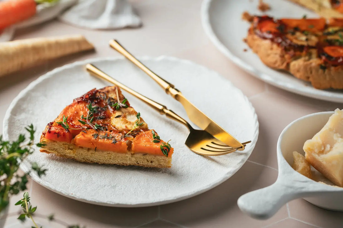 A colorful roasted carrot tart with a golden buckwheat crust, topped with whole roasted carrots and herbs, set on a rustic surface with soft natural lighting 