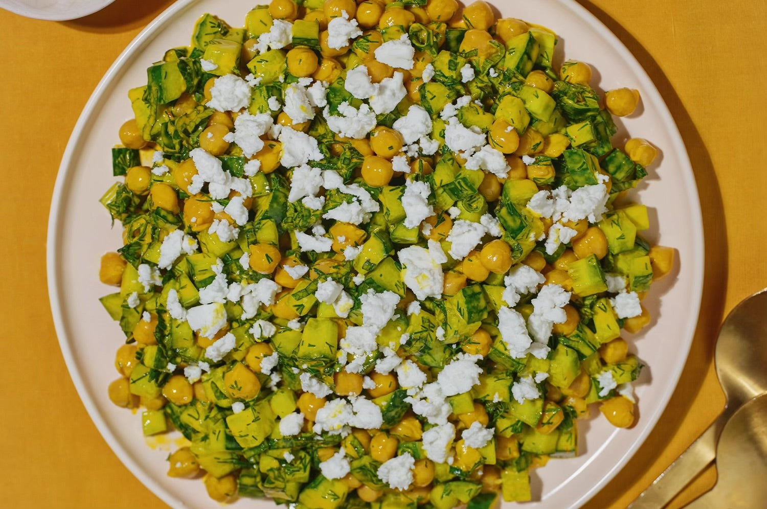 A vibrant herby saffron chickpea salad topped with fresh herbs and citrus, served in a bowl on a neutral surfac