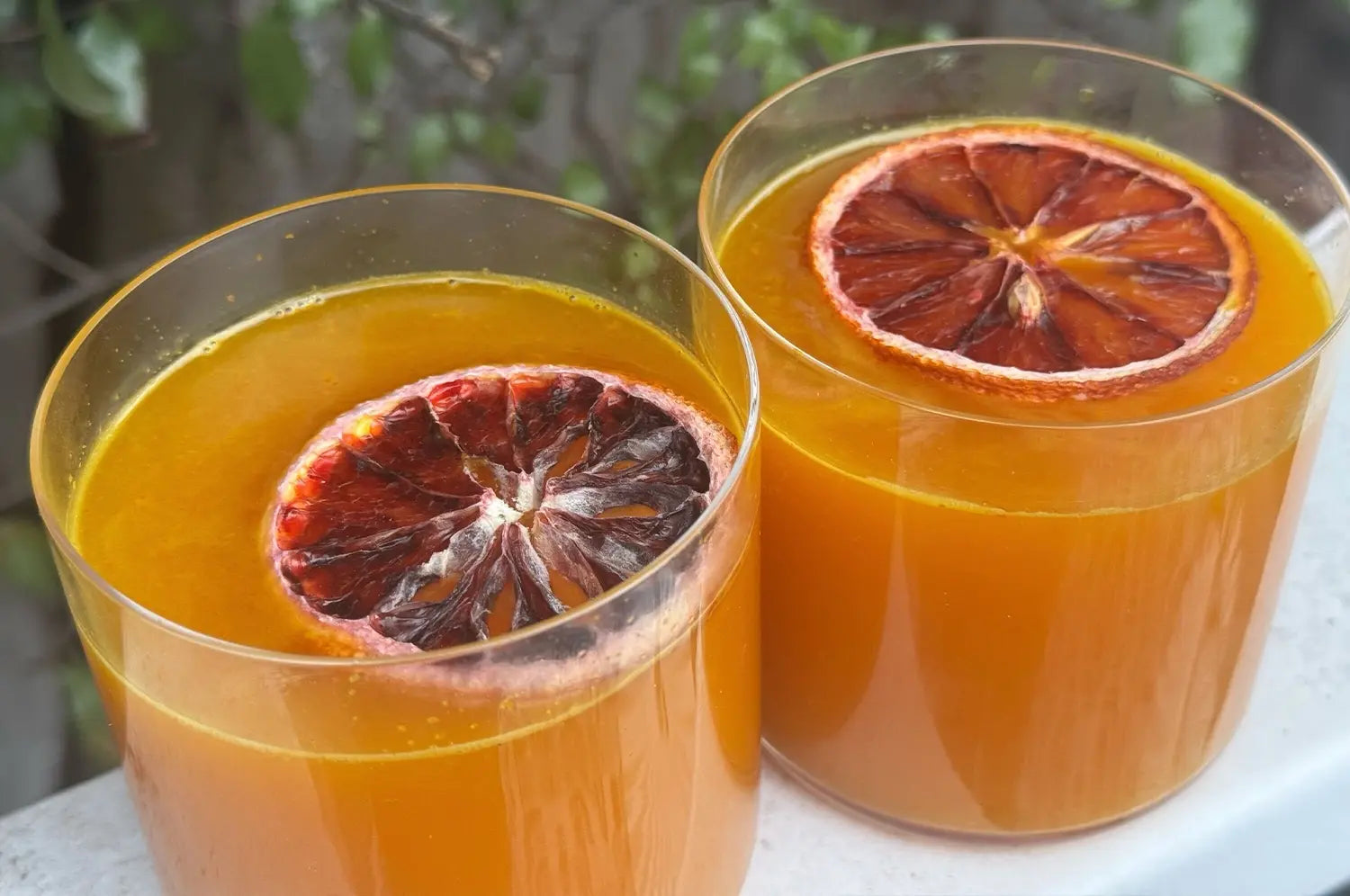 Saffron desert broth with fresh orange slice on top in clear glasses
